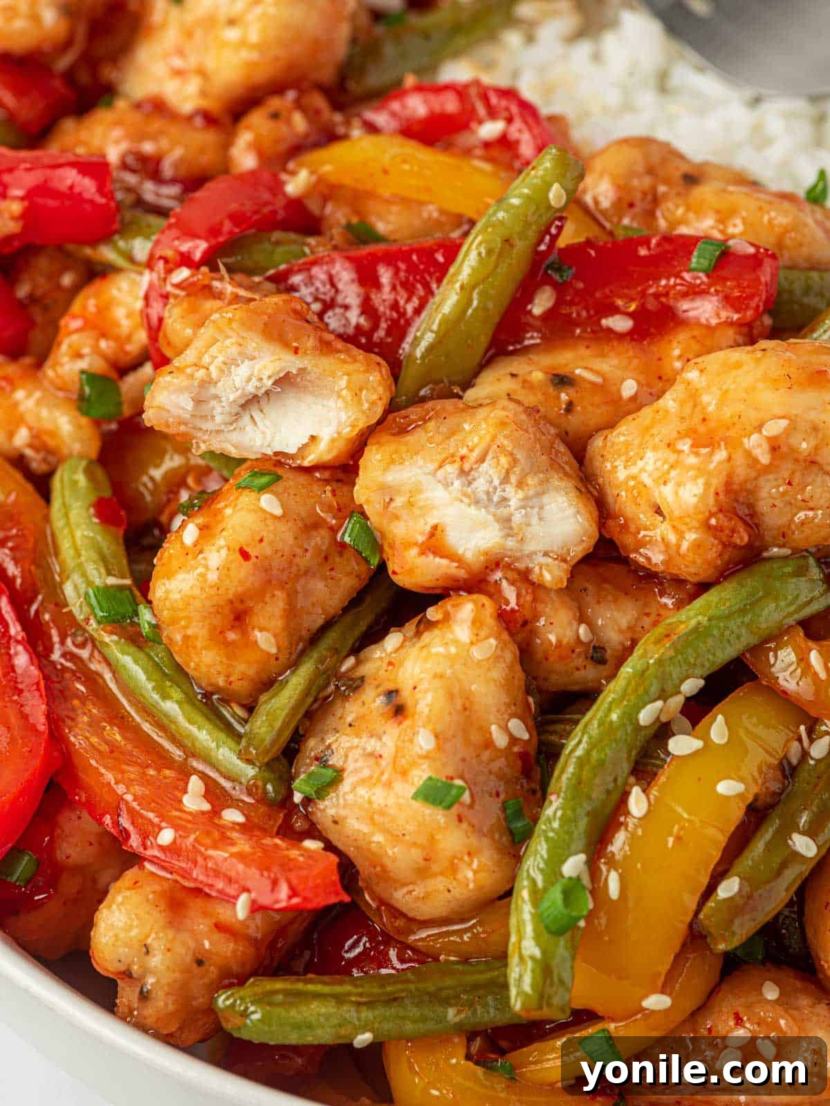A close-up view of succulent crispy chicken coated in sweet chili sauce, mixed with vibrant green beans.