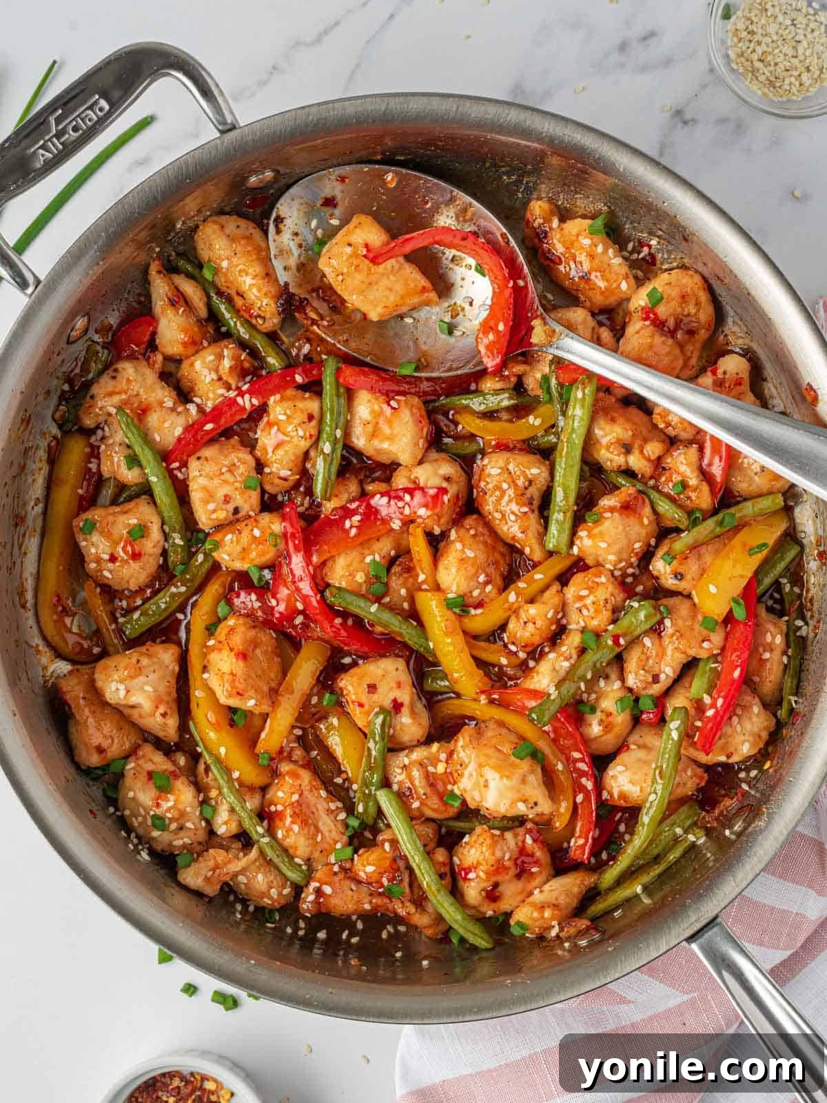 A large skillet filled with sweet Thai chili chicken stir fry, with a serving spoon poised to dish out a delicious portion.