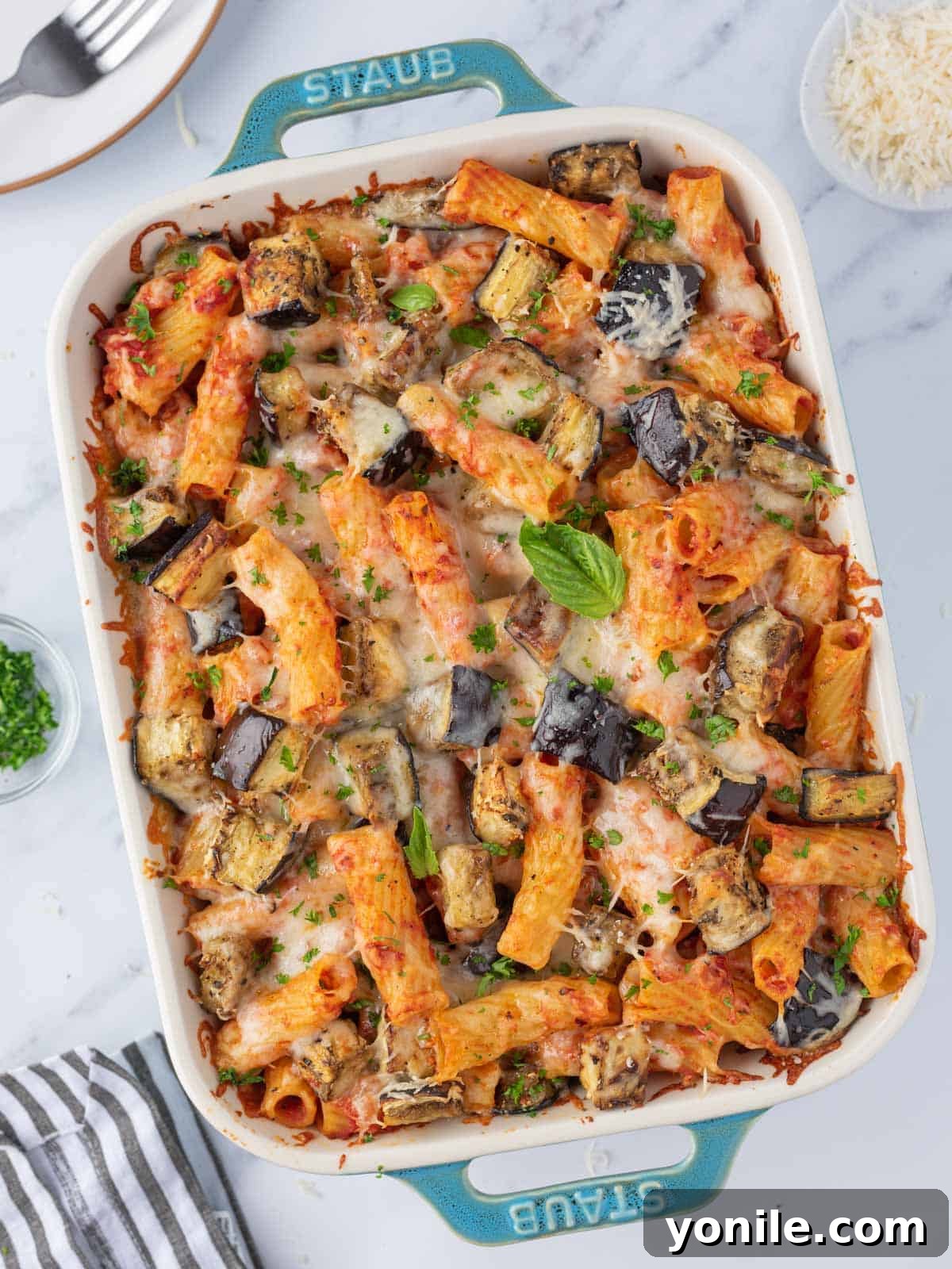Garnished baked eggplant pasta ready to serve, featuring golden-brown cheese and fresh herbs.