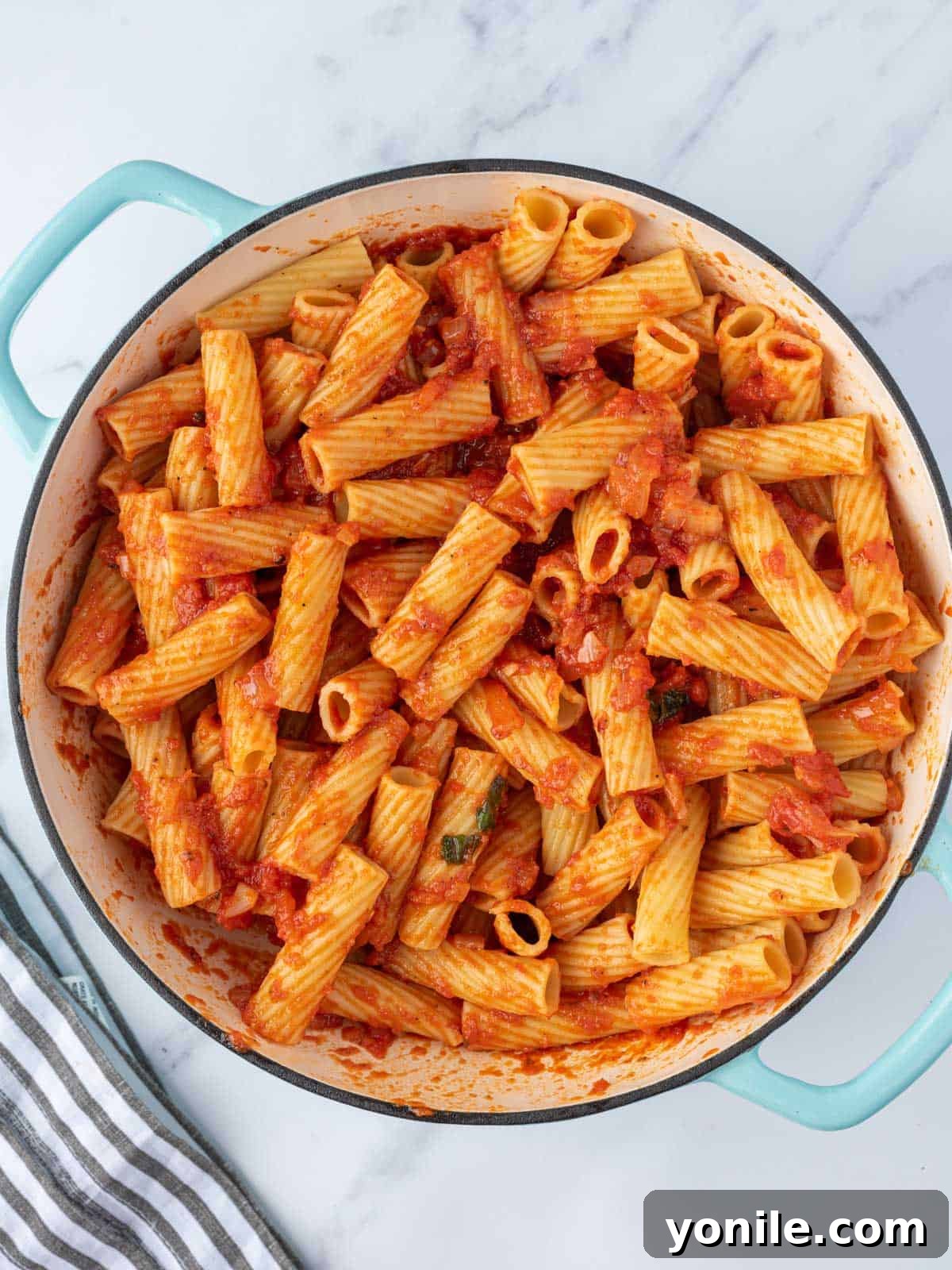 Cooked rigatoni pasta being combined with the spicy Diavolo sauce in a large pot.