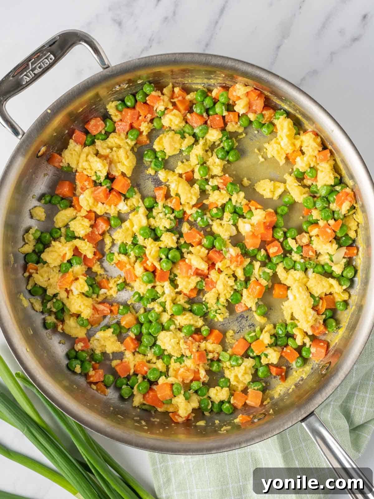 Process of cooking eggs and veggies for Chinese vegetarian fried rice in a skillet.