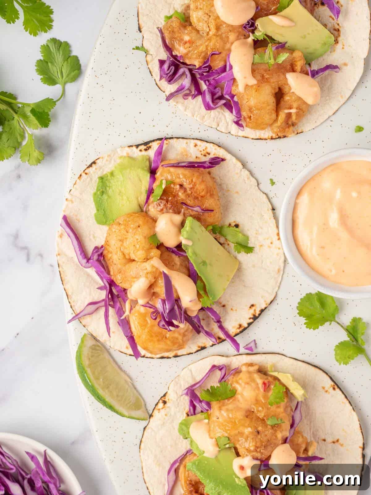 Quickfire Dynamite Shrimp Tacos 2 Three bang bang shrimp tacos with dynamite sauce sit on a serving platter, garnished with cilantro and lime.