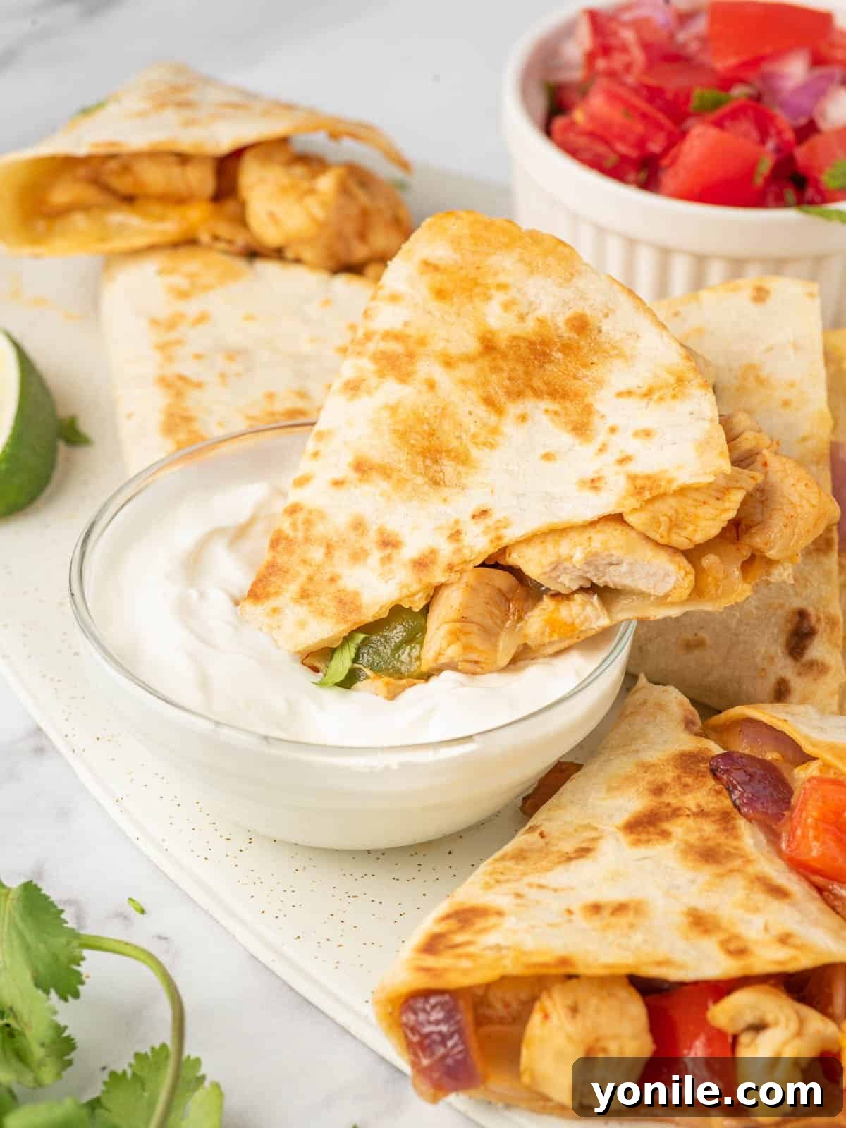 A triangle of chicken and cheese quesadilla being dipped into sour cream.