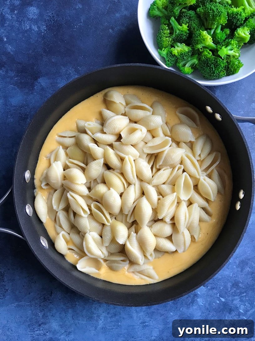 Silky Broccoli Mac 3 Pasta and cheese sauce being stirred in a skillet.
