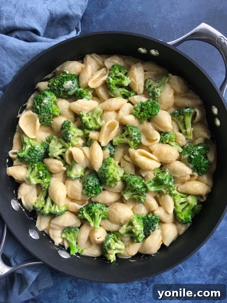 Silky Broccoli Mac 6 Creamy broccoli mac and cheese in a skillet, close-up with a serving spoon.