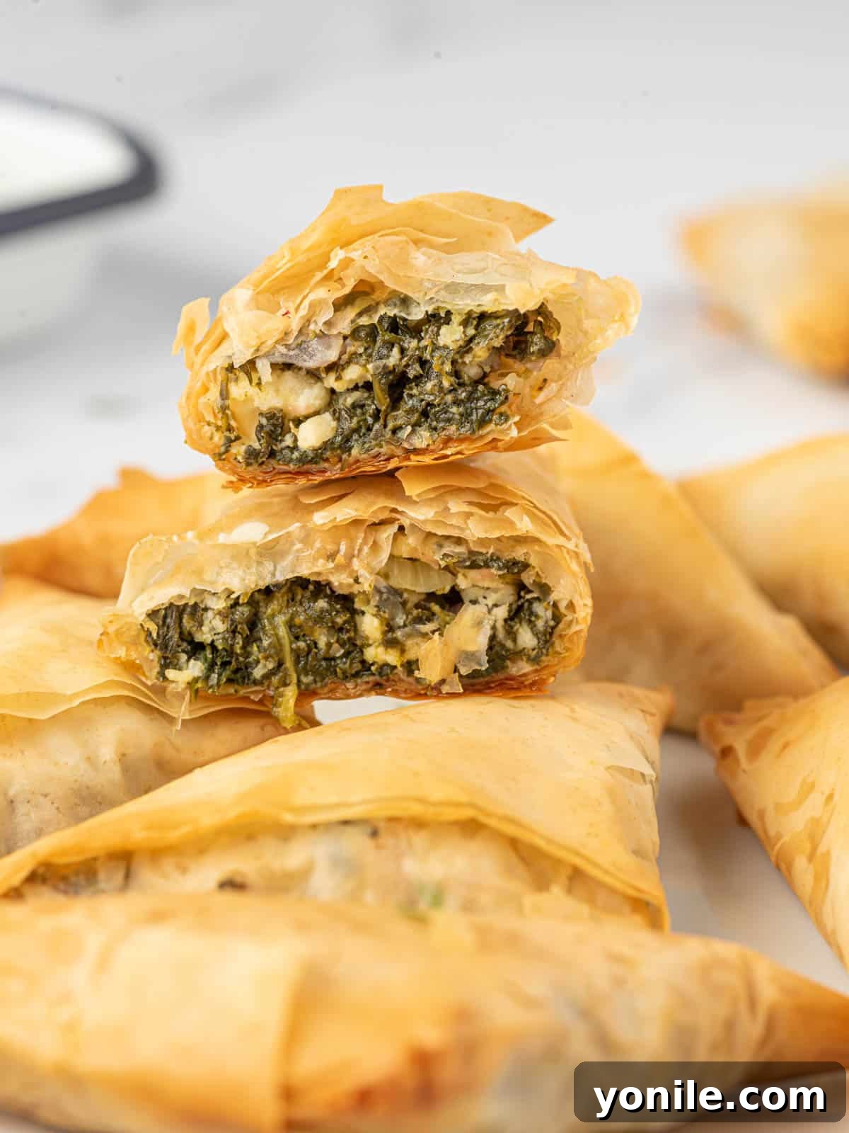 Simple Spanakopita Bites 9 A close-up of handheld Greek spinach pies, cut in half to reveal the savory filling, stacked on a platter.