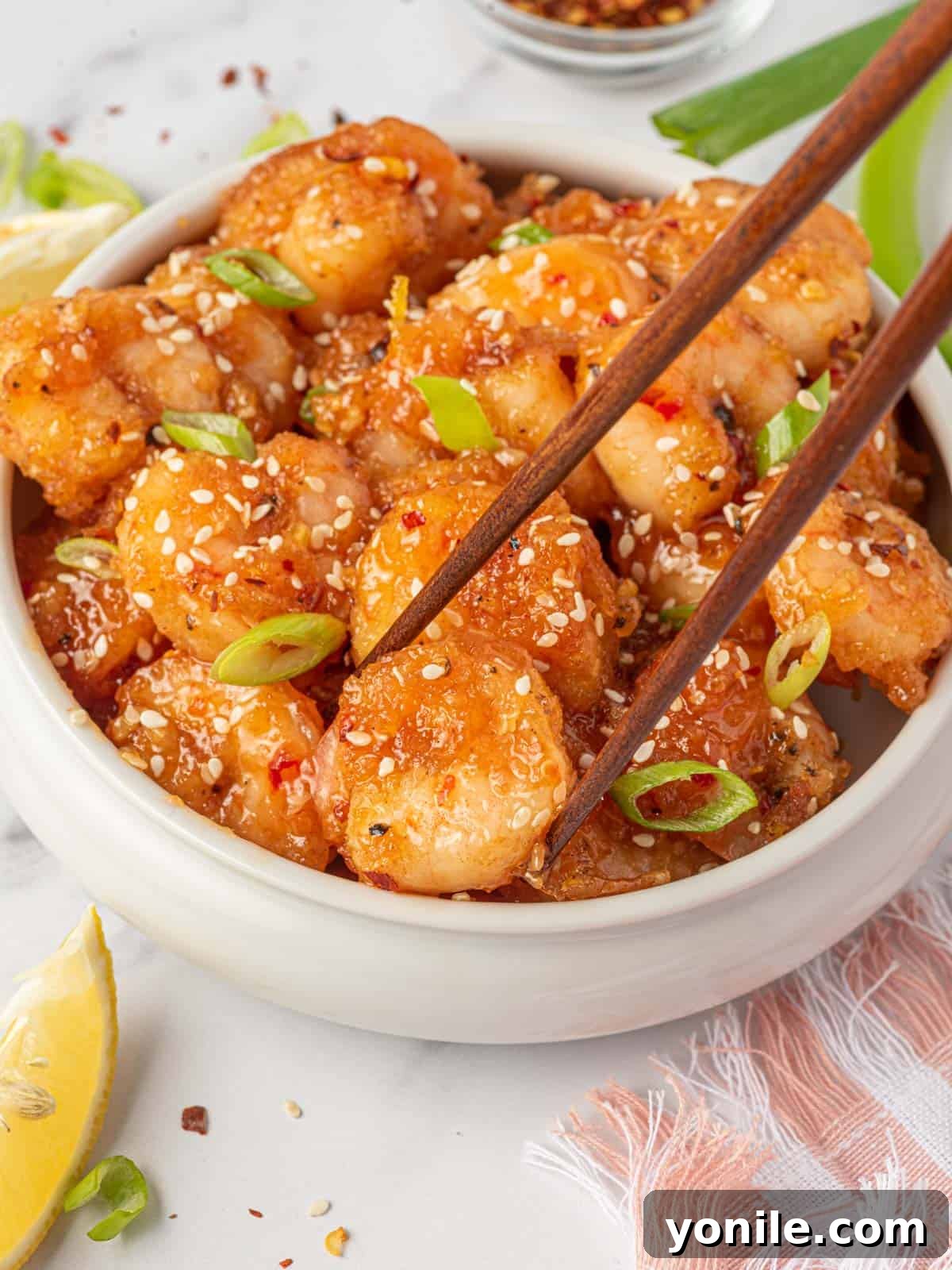 Dynamite Prawns 9 Spicy fried shrimp with firecracker shrimp sauce in a bowl with a piece being picked up by chopsticks.