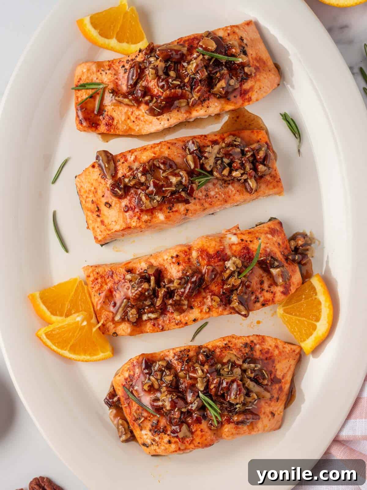 A platter of maple glazed salmon garnished with orange slices and rosemary.