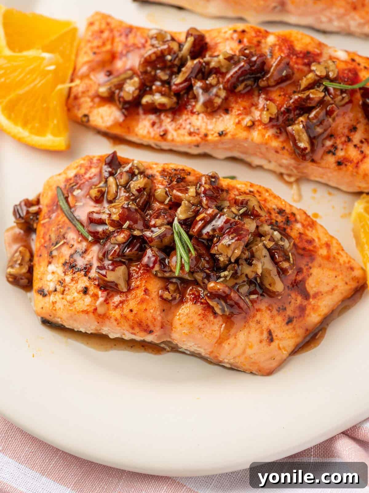 Salmon with maple syrup and pecans on a platter, garnished with fresh oranges and rosemary.
