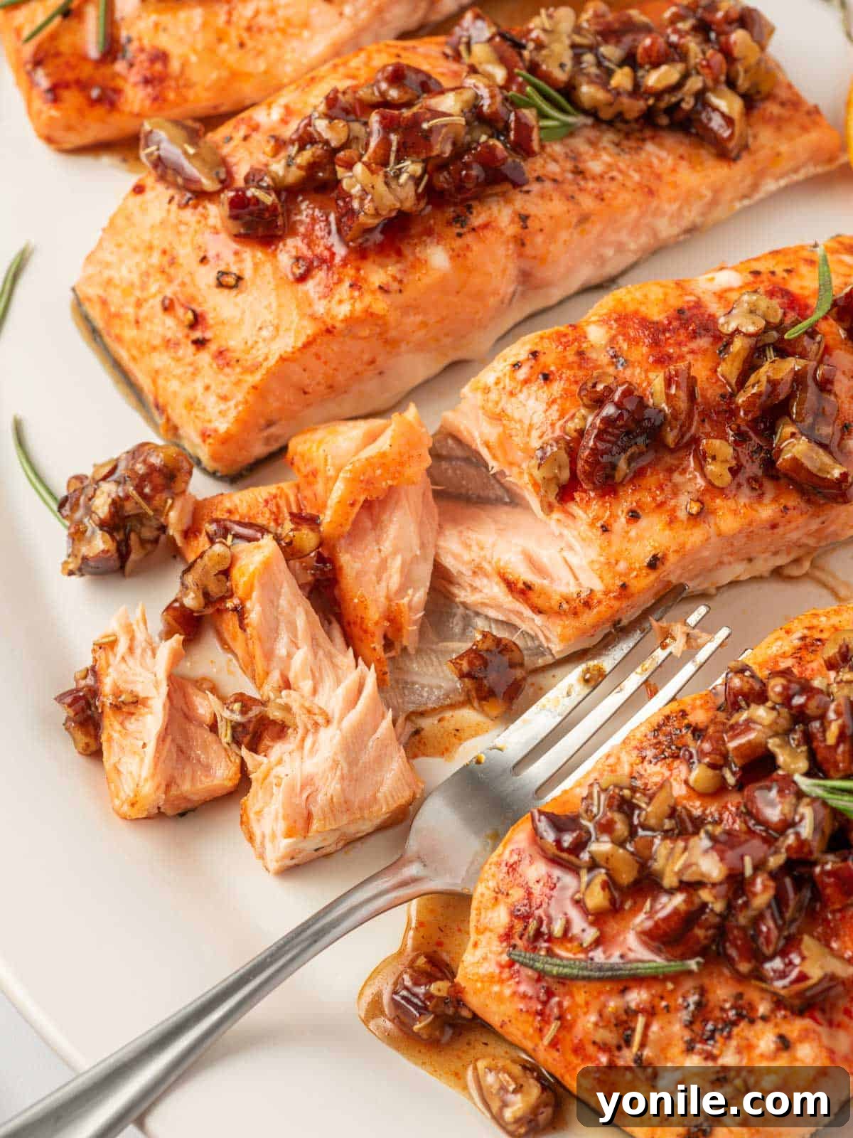 A flaky piece of maple pecan glazed salmon on a plate with a fork, showing its tender interior.