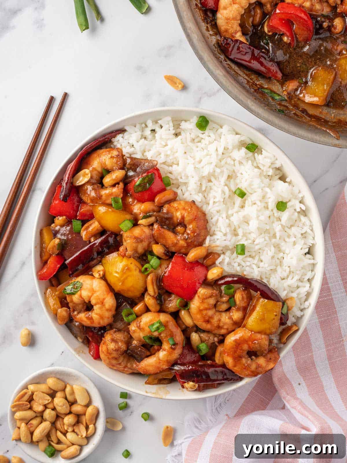Kung pao shrimp recipe in a bowl with rice and chopsticks on the rice.