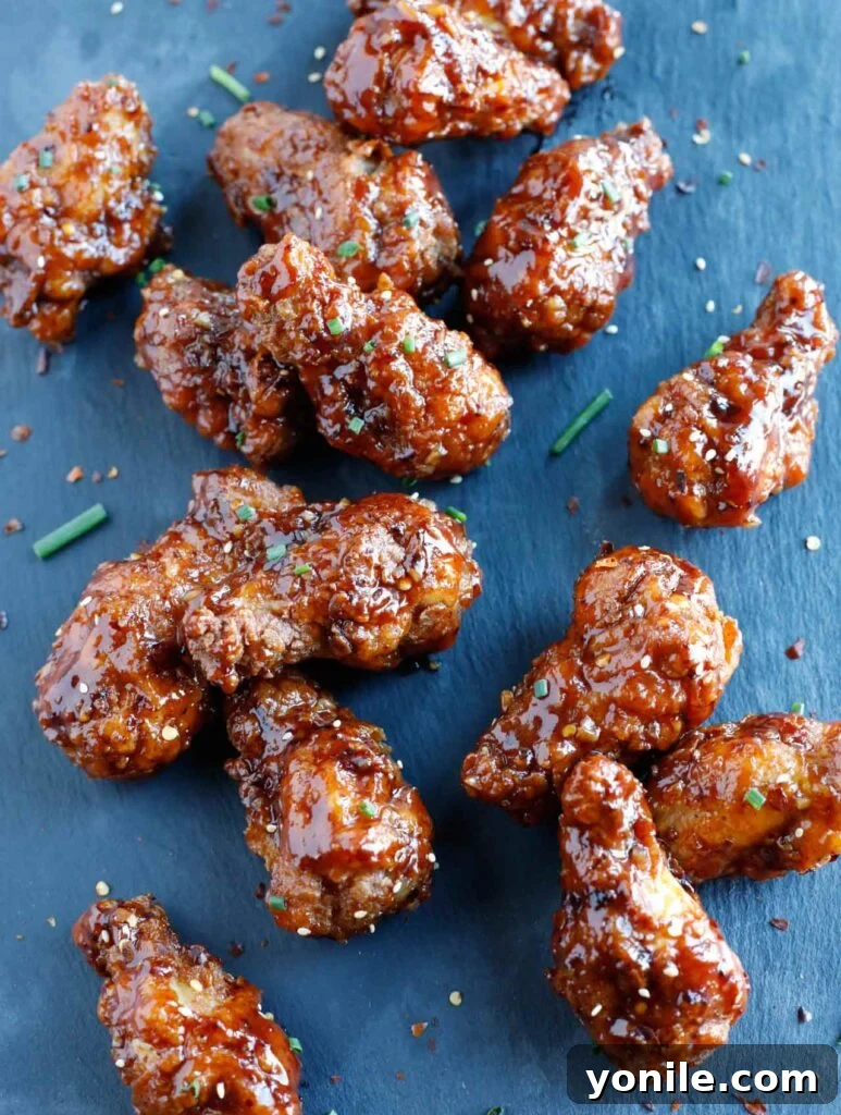 A vibrant platter of golden-brown Honey BBQ Chicken Wings, garnished with fresh chives and toasted sesame seeds, ready to be served.
