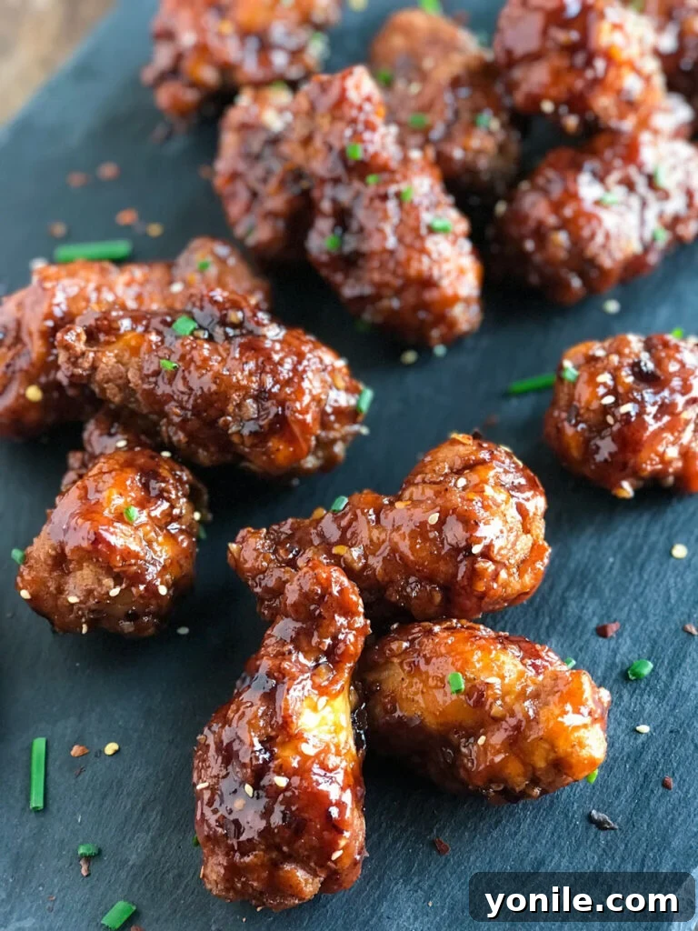 A generous portion of freshly coated Honey BBQ Chicken Wings, glistening with sauce, being tossed in a large bowl.