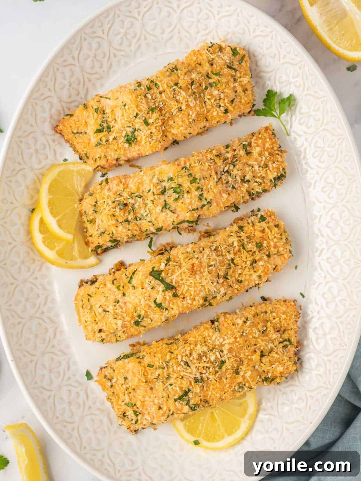 Parmesan crusted salmon recipe on a platter with lemon wedges and fresh herbs.