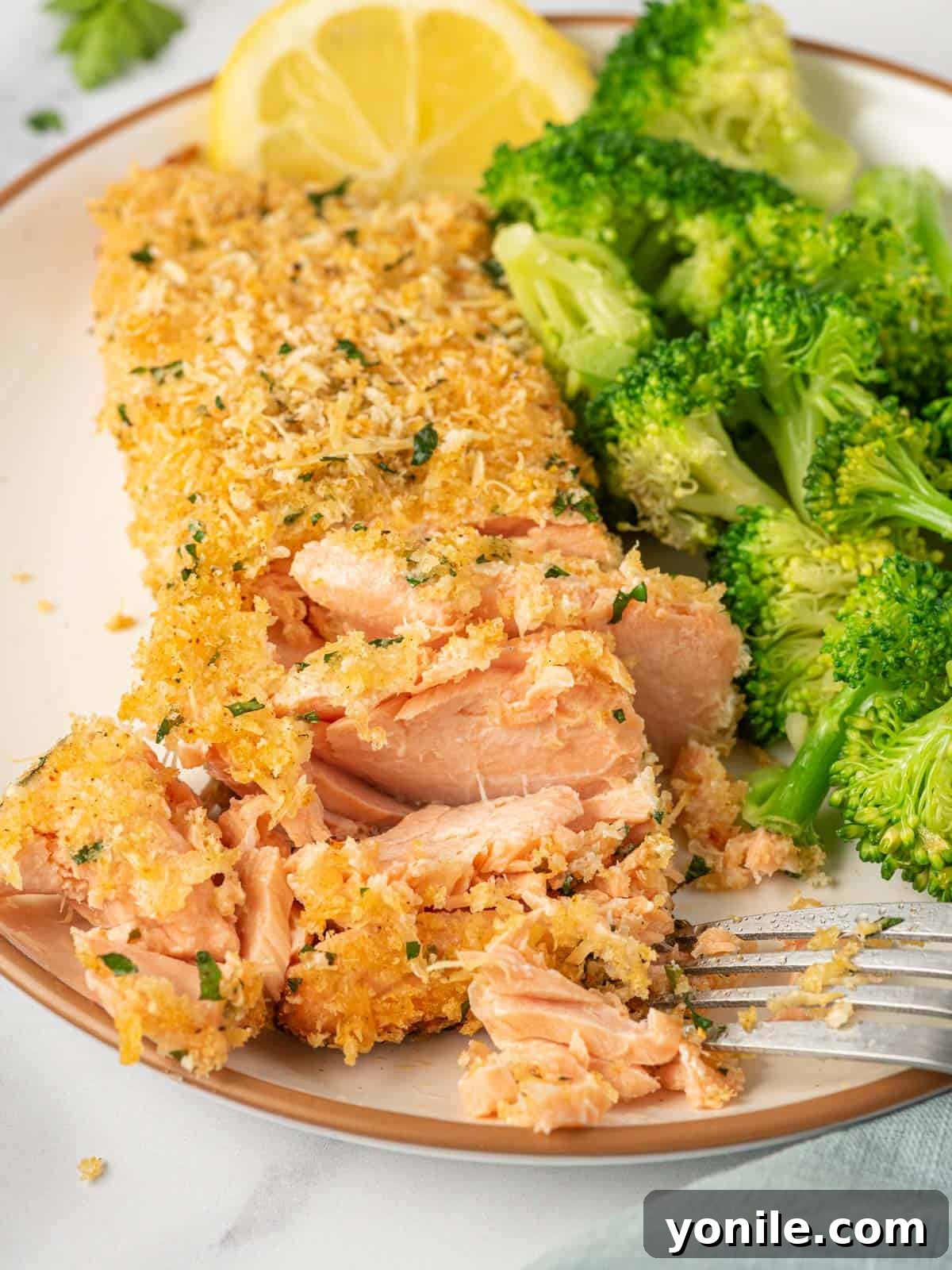 A fork gently flakes a piece of succulent Parmesan crusted salmon, highlighting its tender texture and golden, crispy topping.