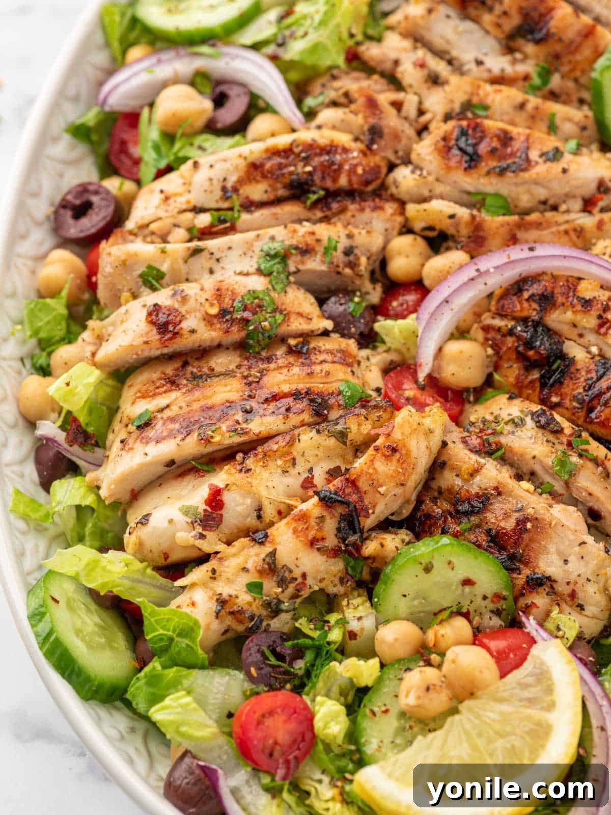 A big platter of mediterranean salad topped with lemon herb chicken.