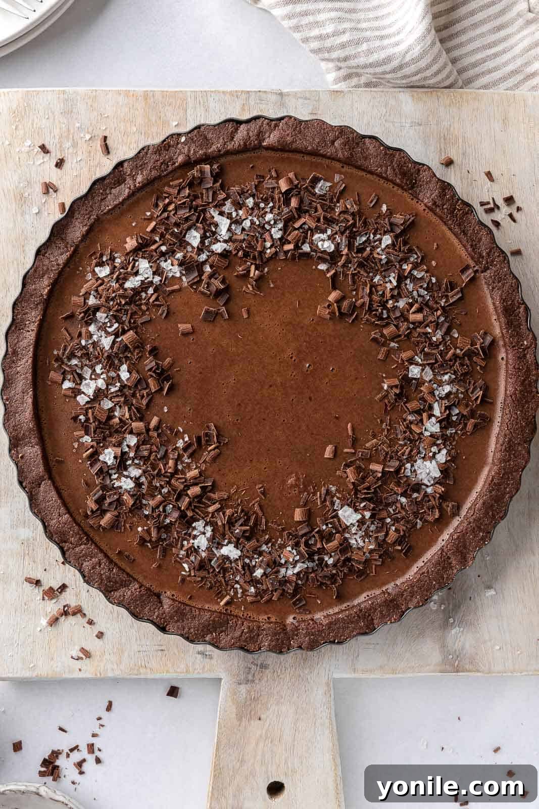 A stunning vegan chocolate pie, beautifully garnished with delicate chocolate shavings and a sprinkle of sea salt, ready to be enjoyed.