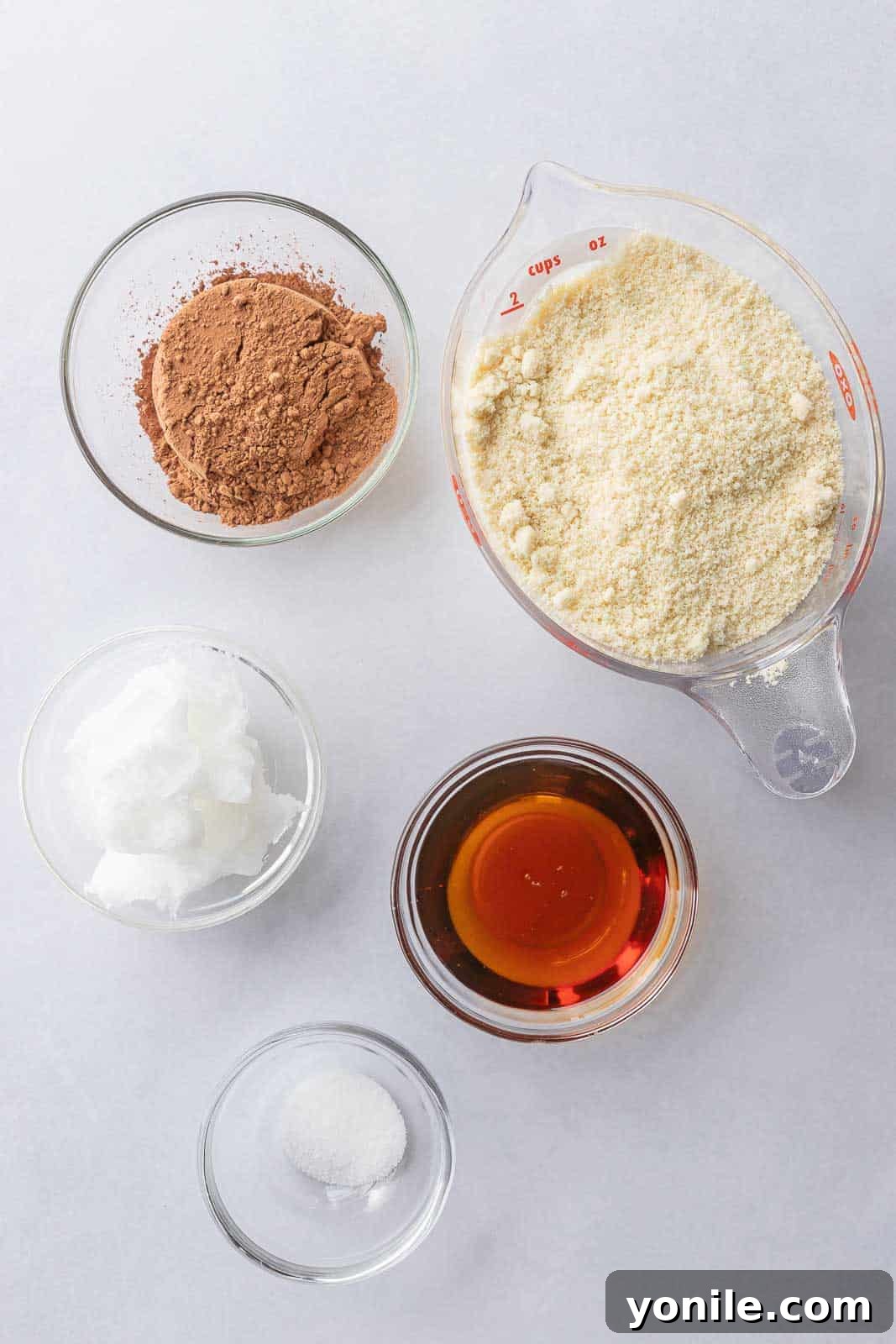All the necessary ingredients laid out to make the best vegan pie crust, including almond flour, cocoa powder, maple syrup, melted coconut oil, and a pinch of salt.