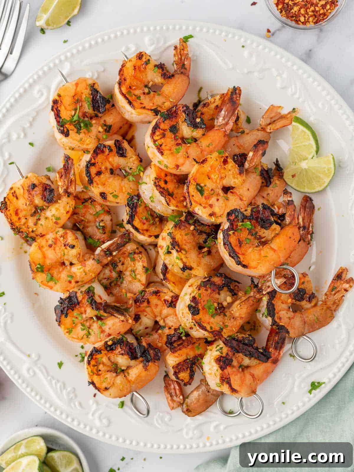 Honey lime shrimp skewers stacked on a plate with fresh lime wedges and parsley for garnish.