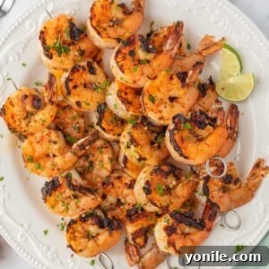 Honey lime shrimp skewers stacked on a plate with lime wedges.