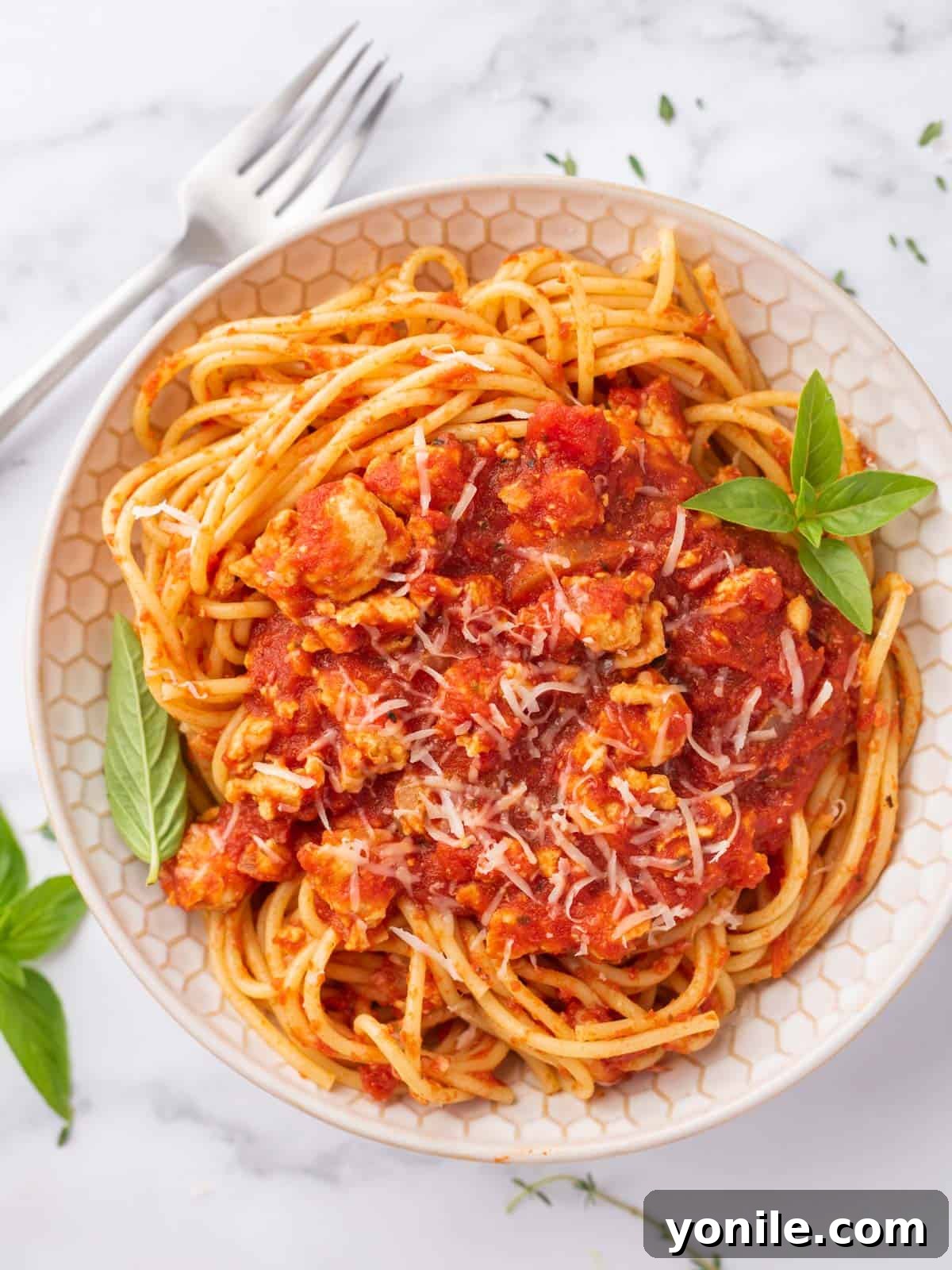 A bowl of healthy chicken bolognese garnished with fresh basil, ready to be served.