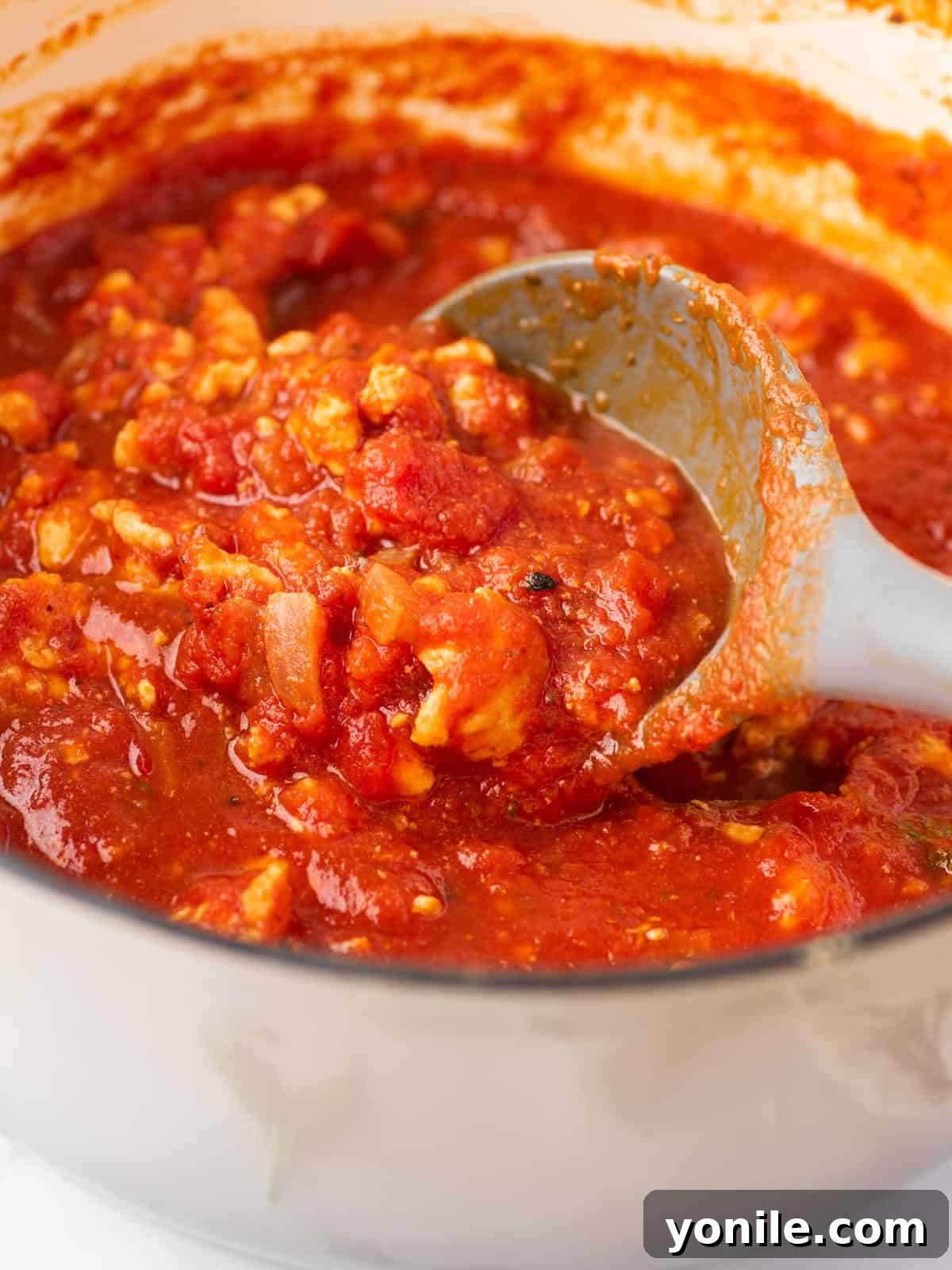A saucepan filled with rich spaghetti sauce with chicken, being stirred with a spoon.
