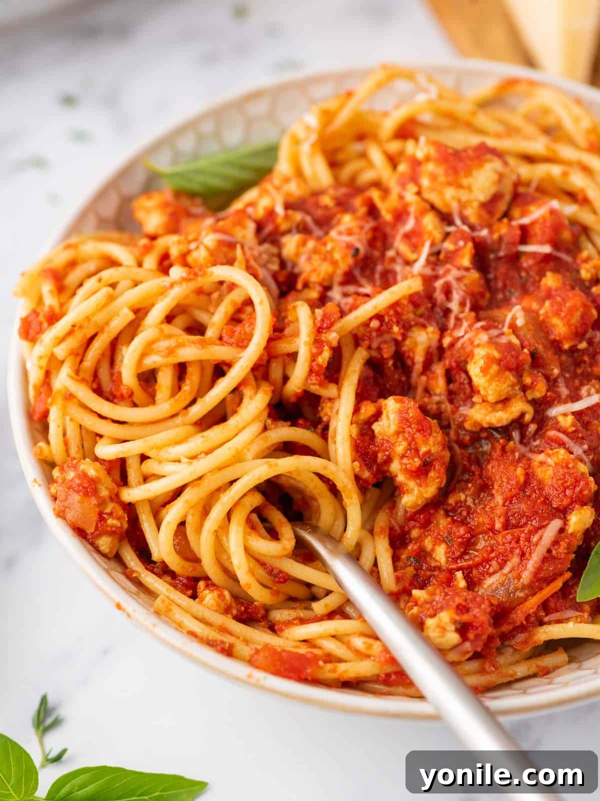 A close-up shot of a fork twirling into a bowl of perfectly cooked ground chicken bolognese.