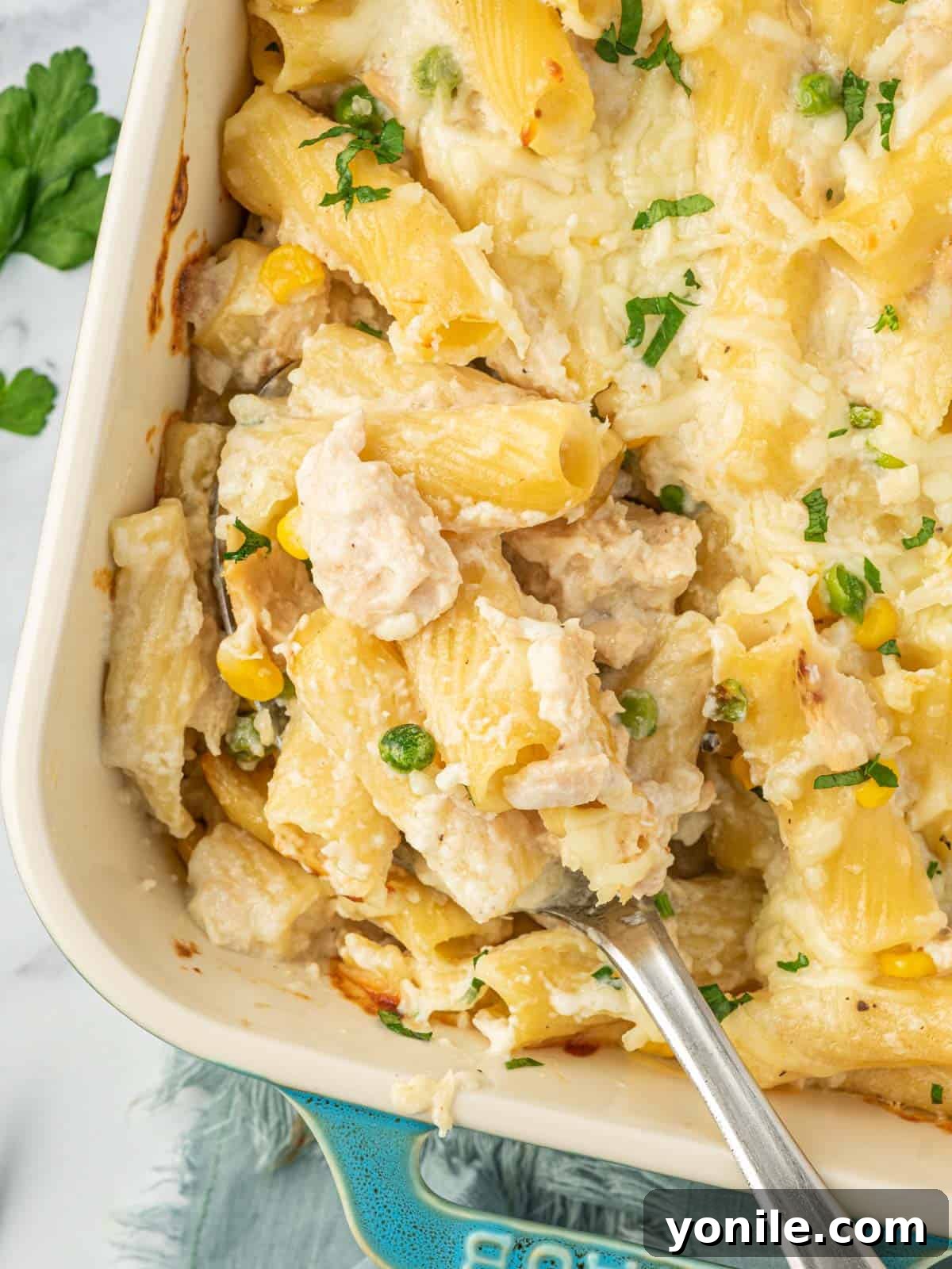 Velvety Tuna Pasta Casserole 10 A spoon scoops a generous serving of cheesy tuna bake from the dish.