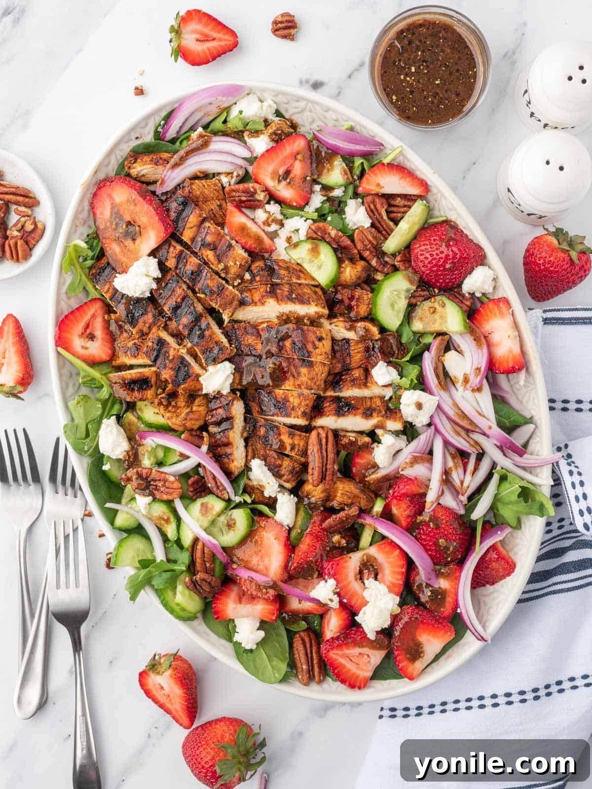 A large platter of spinach salad with strawberries and balsamic grilled chicken with several forks on the side.