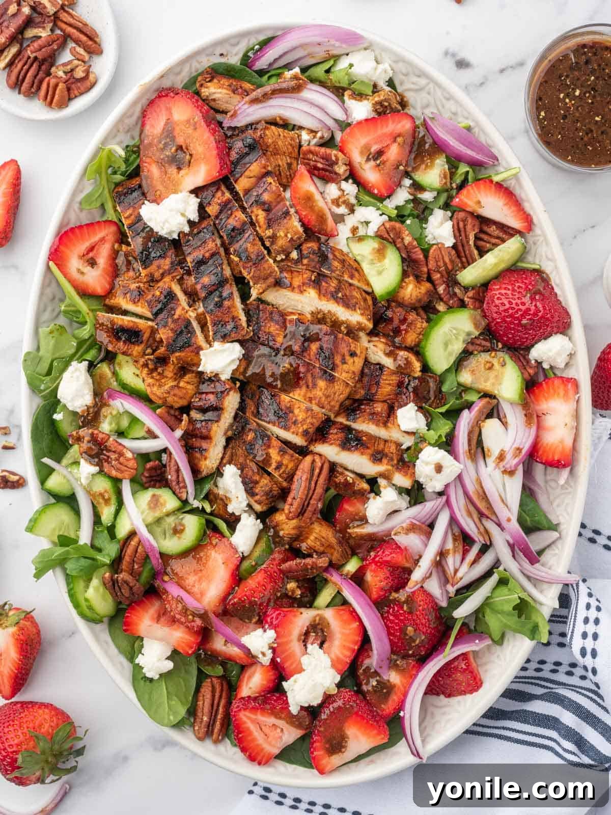 Grilled chicken on spinach salad with fresh strawberries on a serving platter with balsamic dressing and pecans to the side.