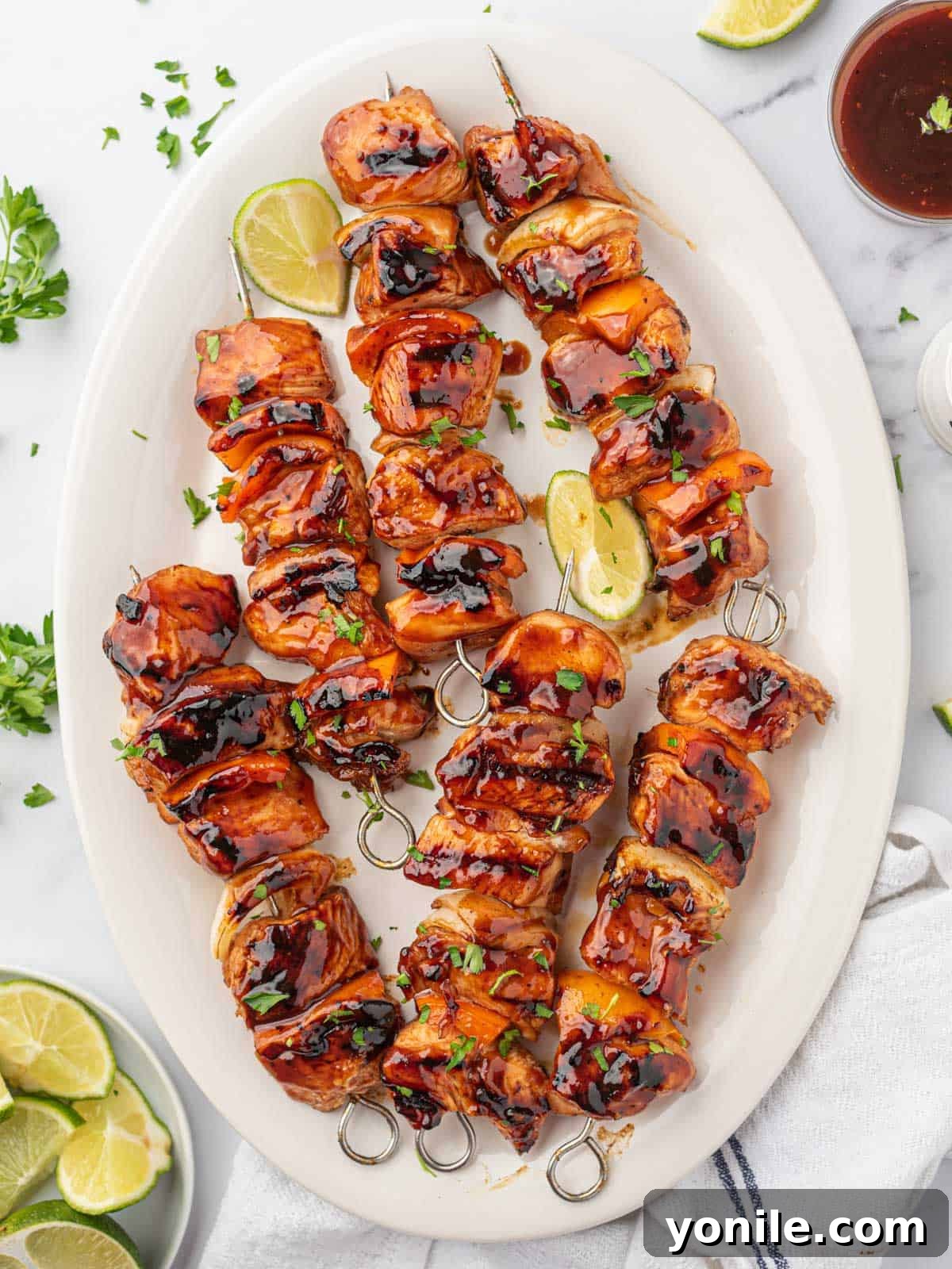 The Ultimate BBQ Chicken Skewers 2 Honey BBQ chicken kabobs artfully arranged on a platter with fresh lime wedges for garnish.
