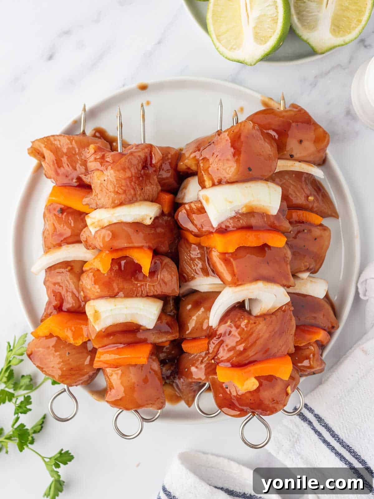 The Ultimate BBQ Chicken Skewers 5 Honey BBQ chicken kabobs and colorful vegetables neatly prepped for grilling and stacked on a plate.