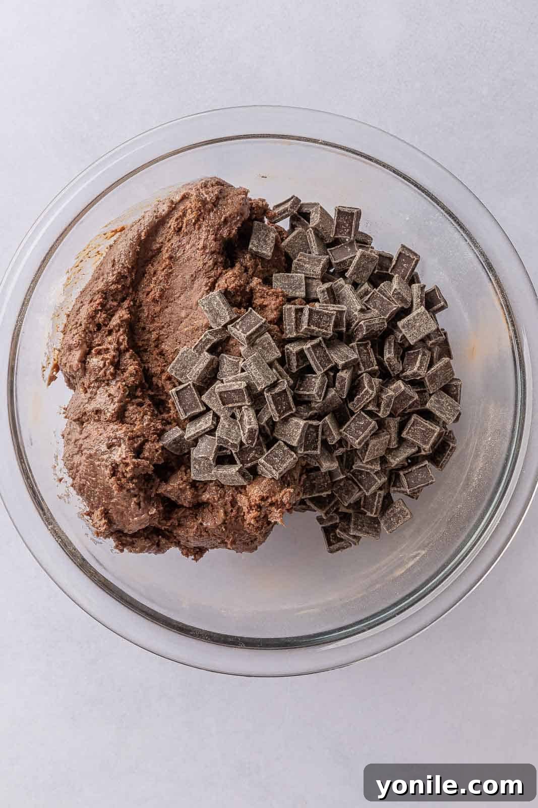 Close-up of mixing vegan chocolate chips and chunks into the prepared plant-based cookie batter, ensuring an even distribution.
