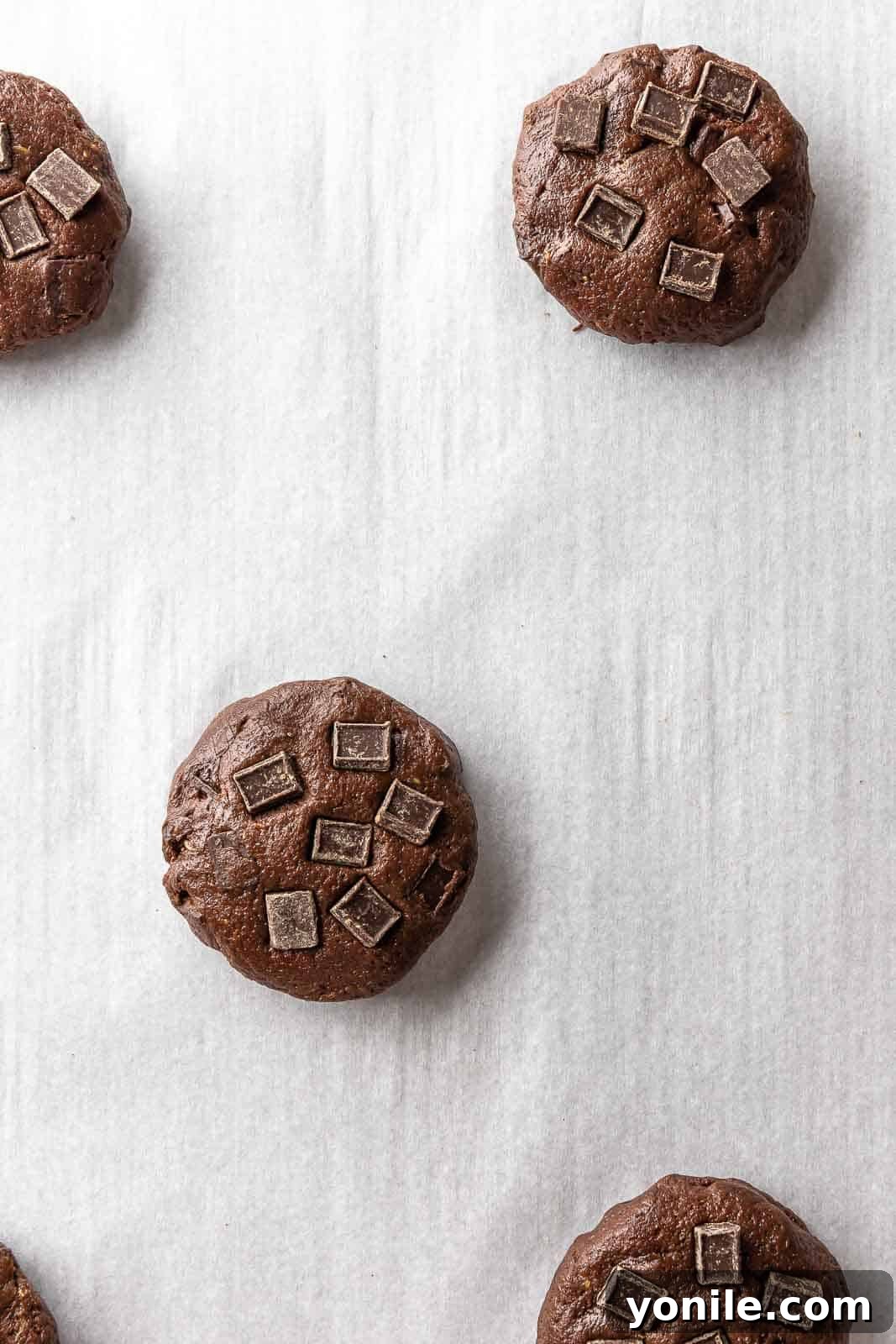 Neatly portioned balls of unbaked vegan chocolate chip cookie dough, ready for the oven on parchment paper.
