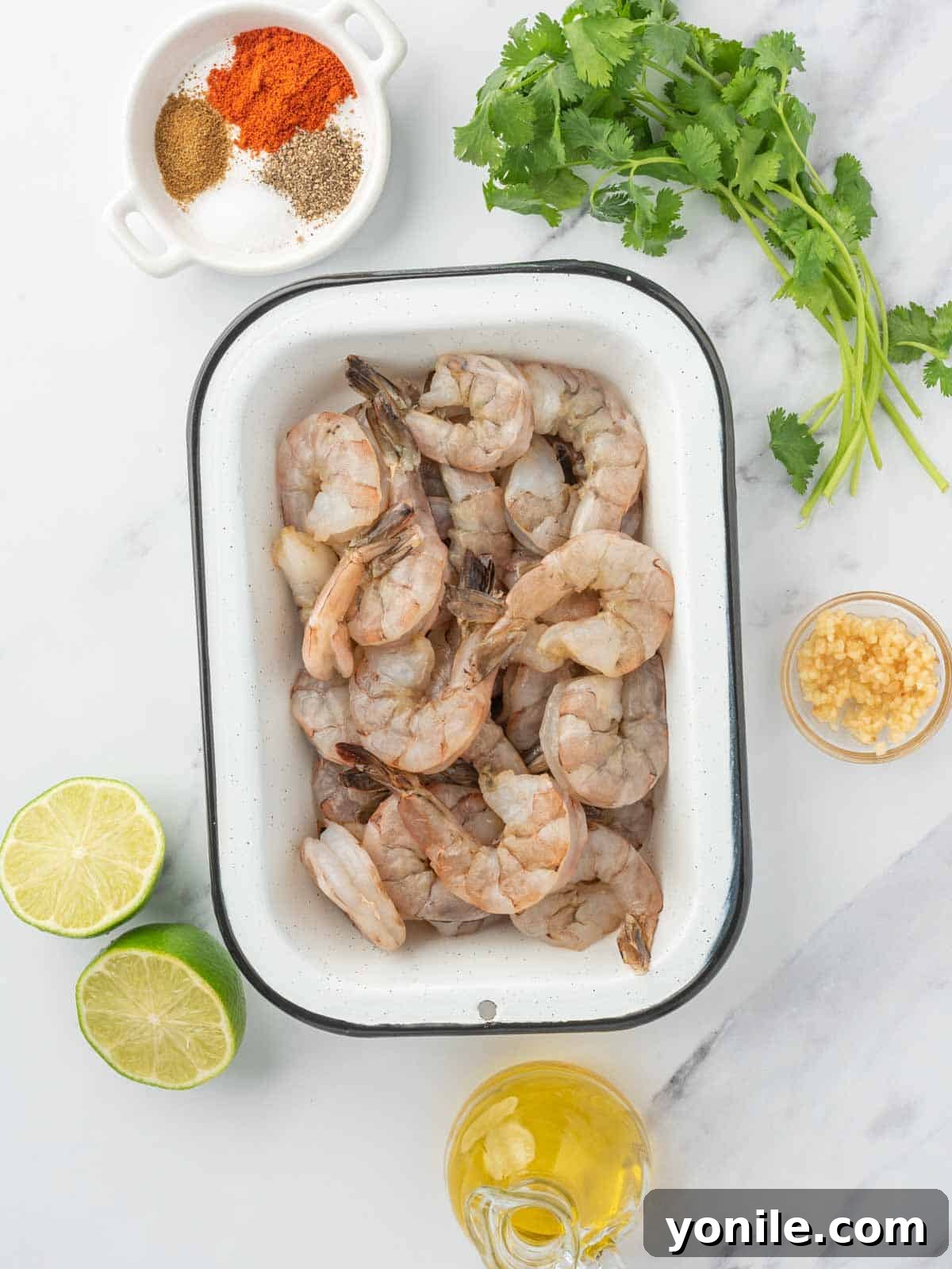 Fresh ingredients laid out for making chili lime shrimp, including limes, cilantro, garlic, olive oil, spices, and jumbo shrimp.