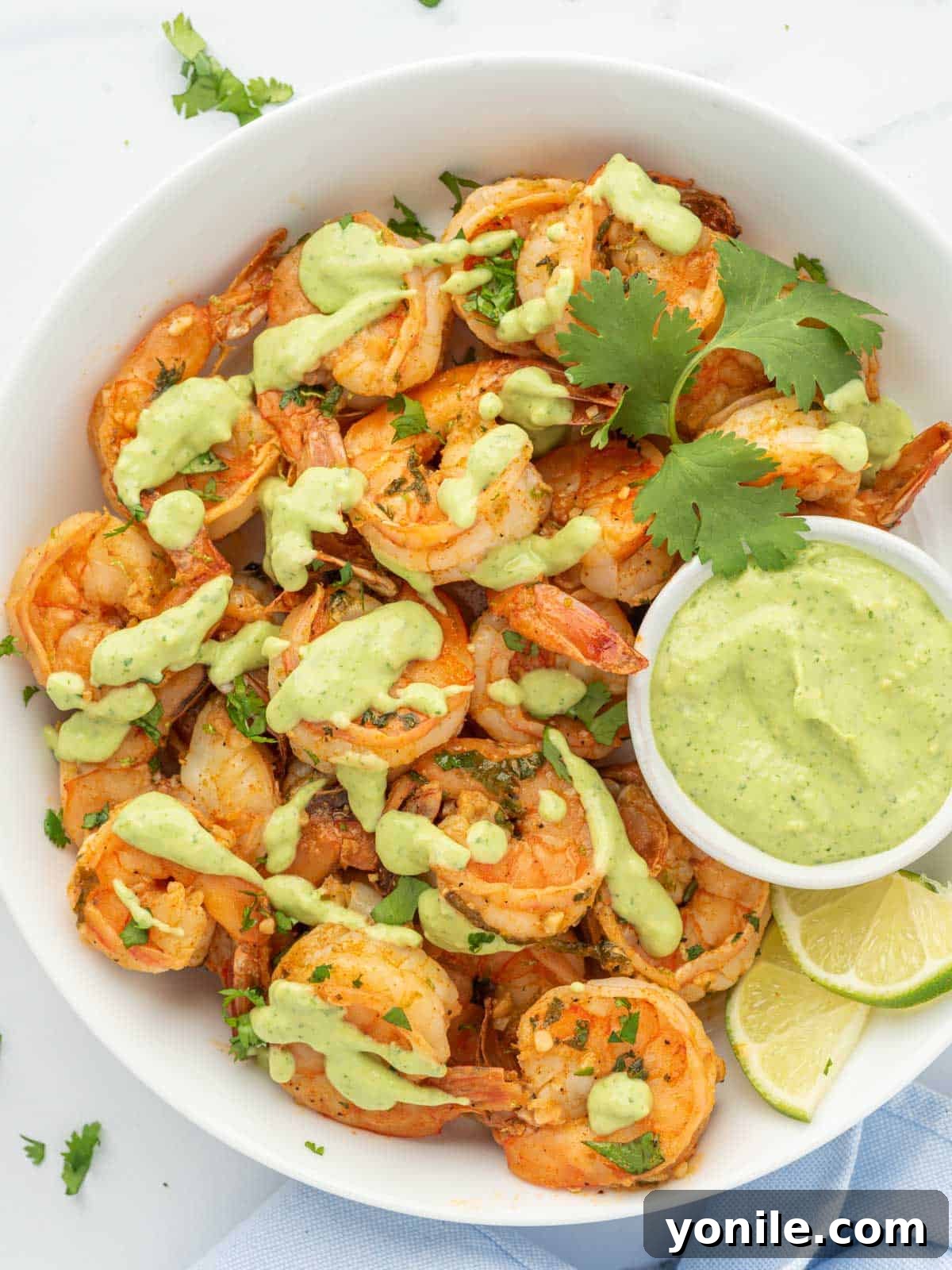 Platter of vibrant Chili Lime Shrimp with a side of green aioli for dipping, garnished with fresh cilantro and lime wedges.