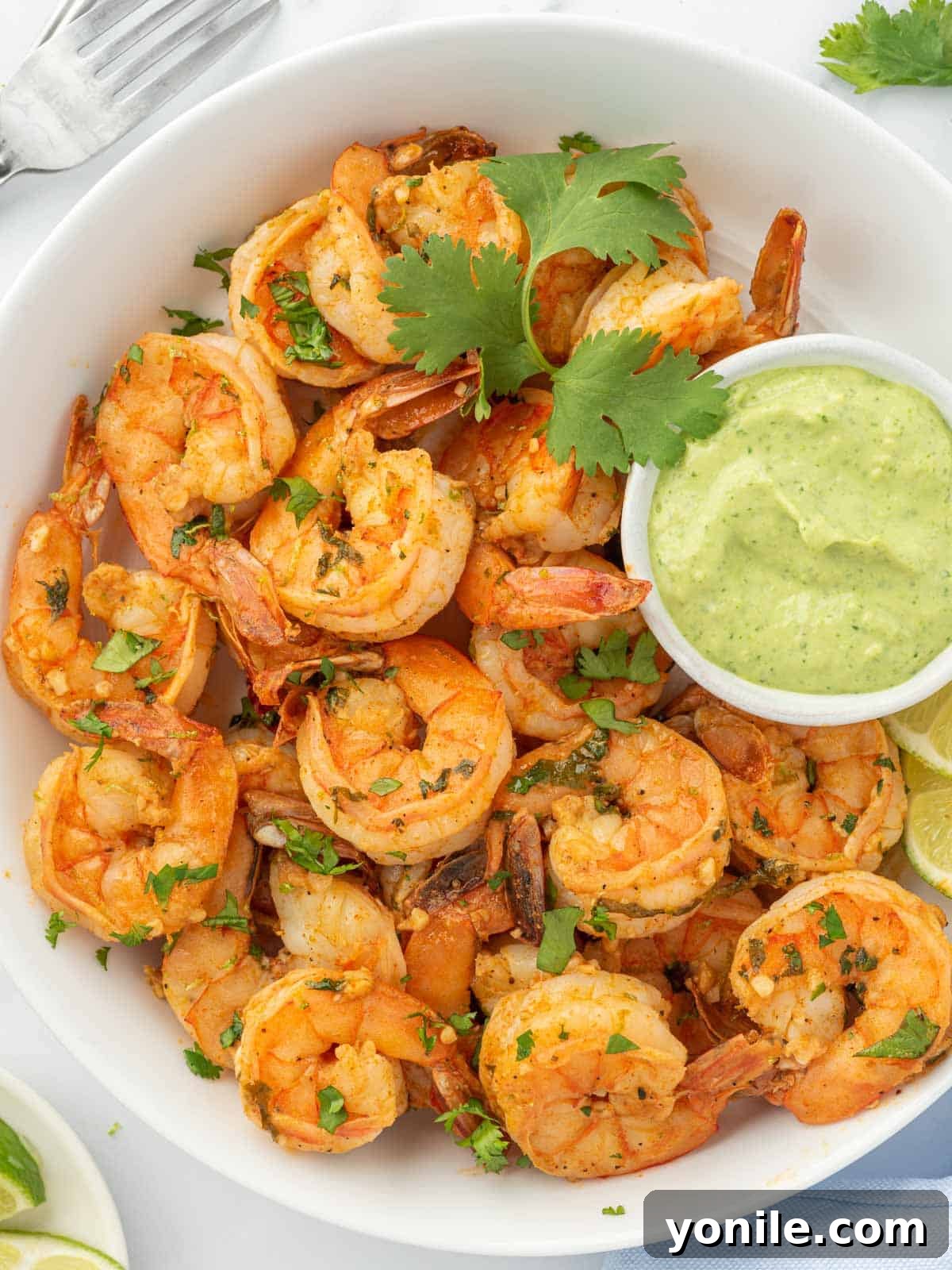 A vibrant serving bowl of cooked shrimp with cilantro and lime, accompanied by a small bowl of green aioli for dipping.