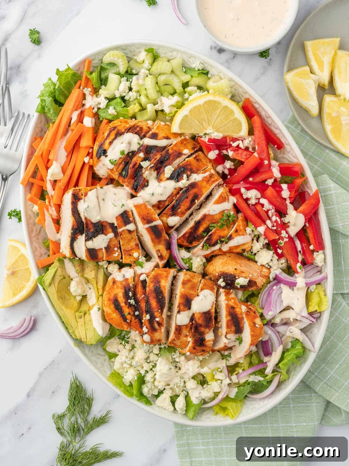 A platter of salad with buffalo chicken, featuring grilled chicken breast pieces, vibrant vegetables, and creamy dressing.