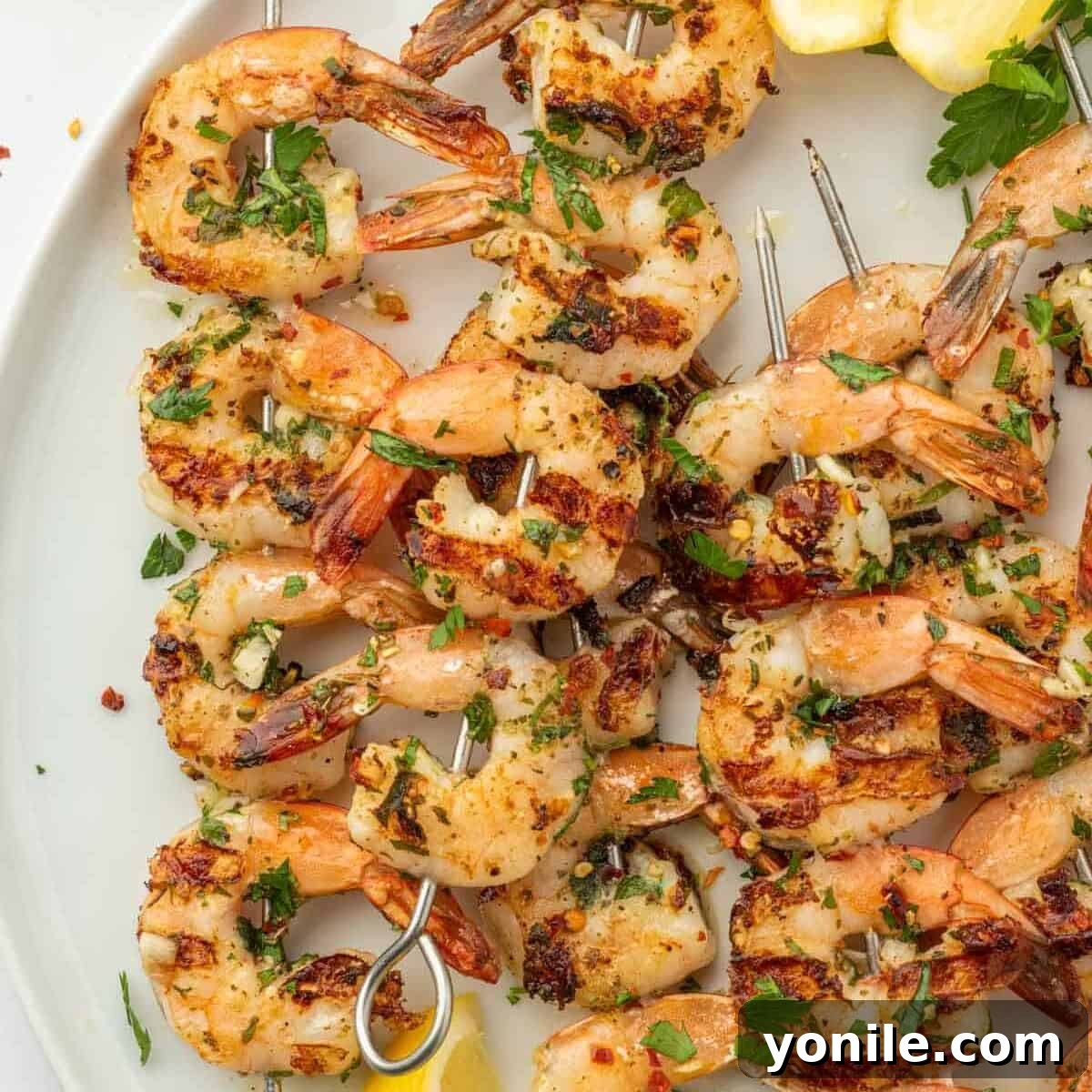 Grilled garlic shrimp kabobs arranged on a white platter, garnished with fresh lemon wedges, ready to serve.