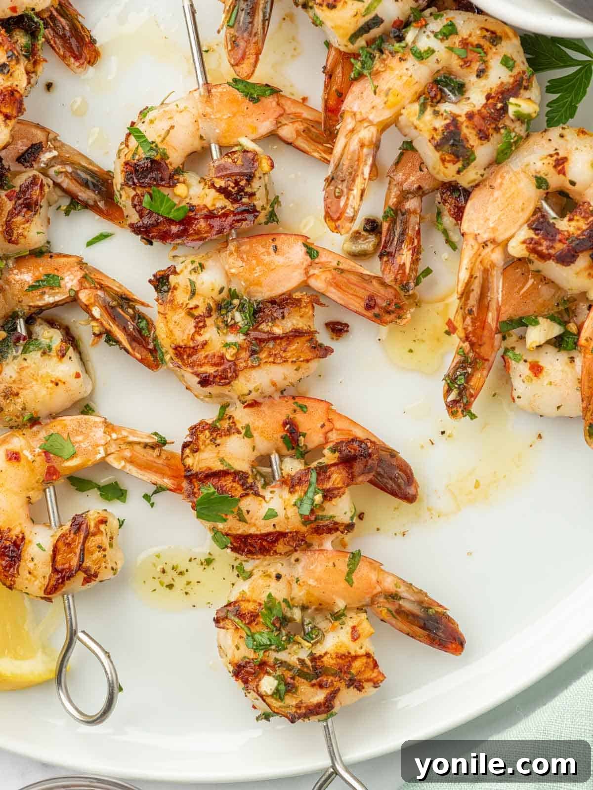 Close-up of three grilled garlic shrimp skewers served on a rustic white plate, ready for dining.