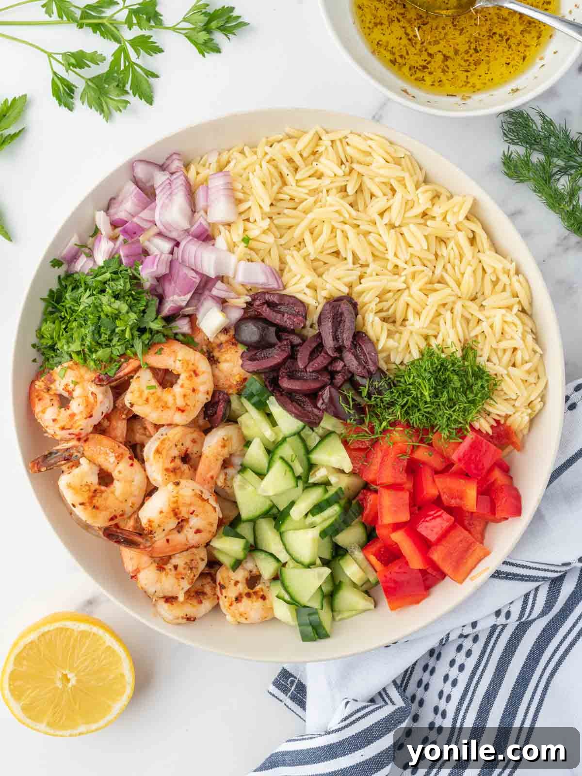 Mediterranean Shrimp Orzo Salad 7 A chef's hands assembling an orzo salad with grilled shrimp, bell peppers, cucumber, and olives in a large serving bowl.