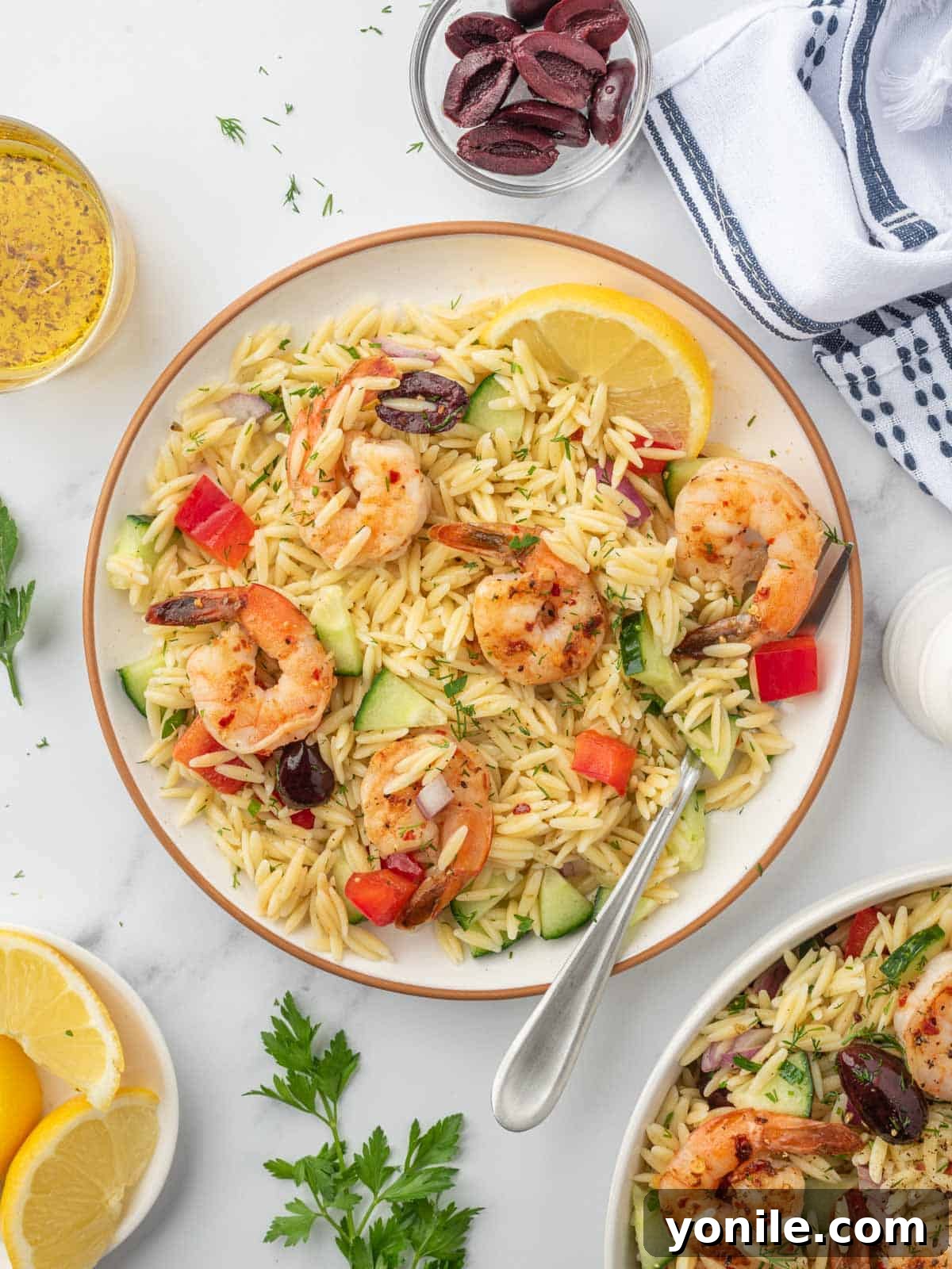 Mediterranean Shrimp Orzo Salad 8 A portion of shrimp orzo salad artfully arranged on a white plate with a fork resting beside it, garnished with fresh herbs.