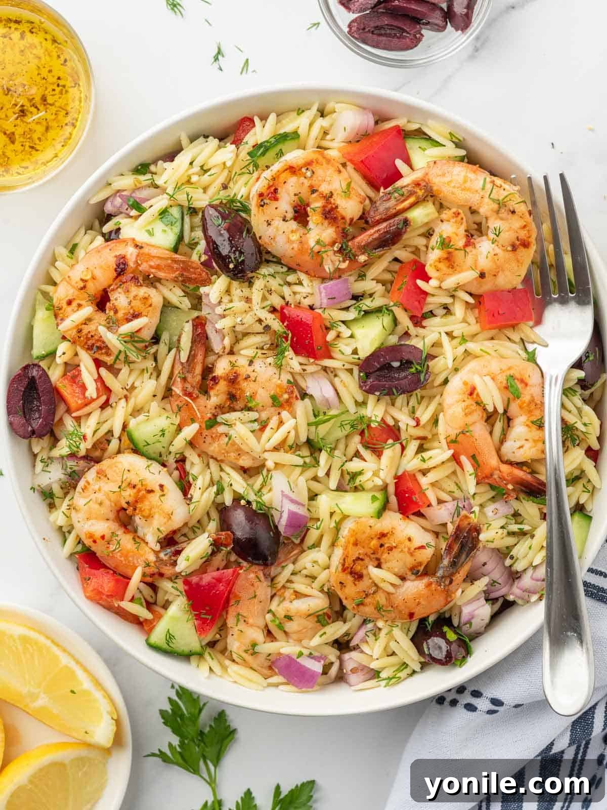 Mediterranean Shrimp Orzo Salad 9 A fork rests on the side of a bowl filled with a generous serving of colorful orzo salad topped with grilled shrimp, ready to be enjoyed.