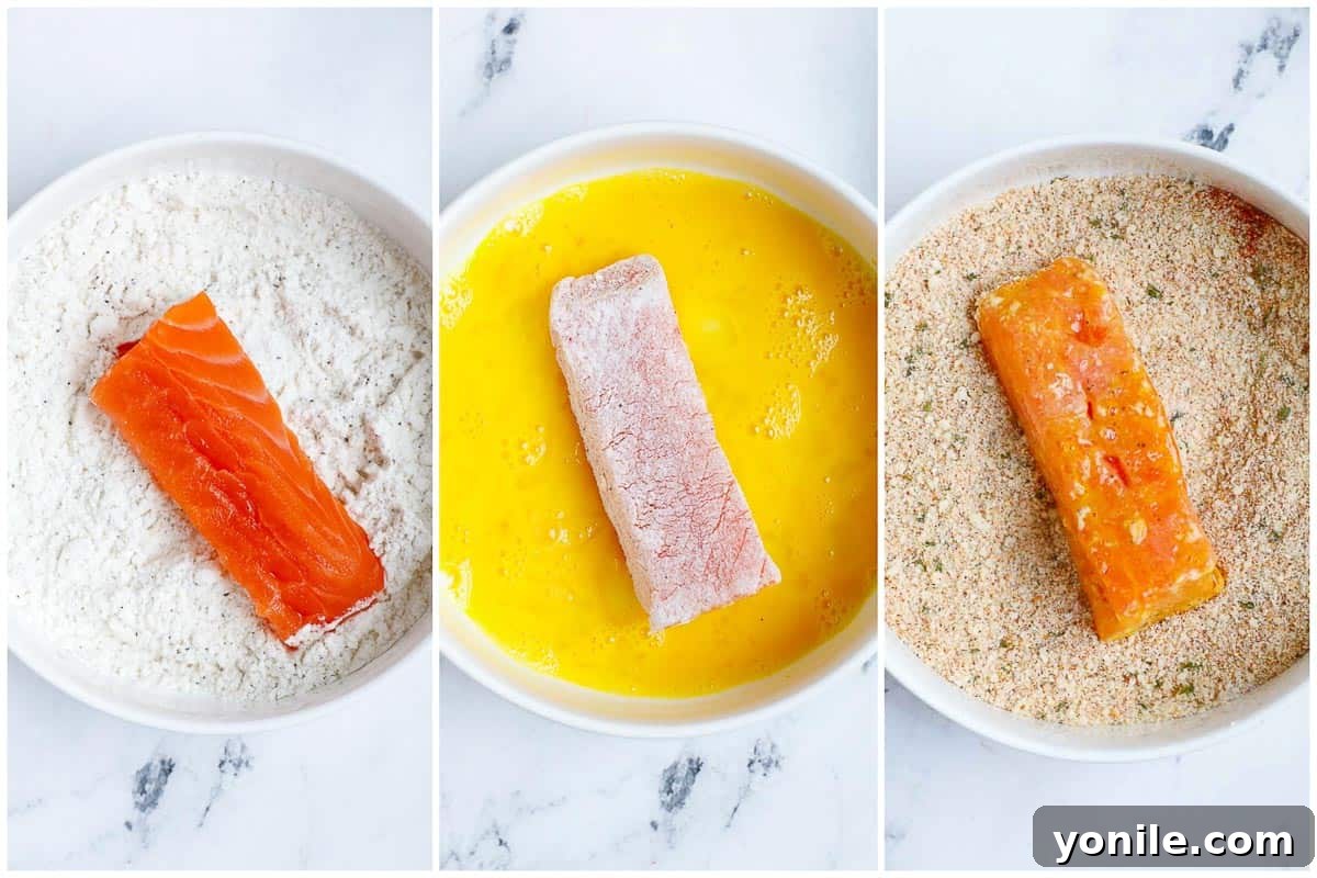 A close-up view demonstrating the dredging process, where a salmon stick is coated first in flour, then egg wash, and finally pressed into a bowl of panko breadcrumbs for a complete coating.