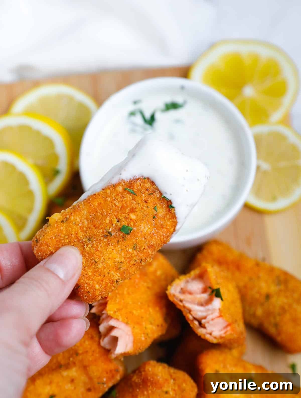 A close-up shot of a single perfectly breaded and baked salmon fish stick, showcasing its golden crust and flaky interior.