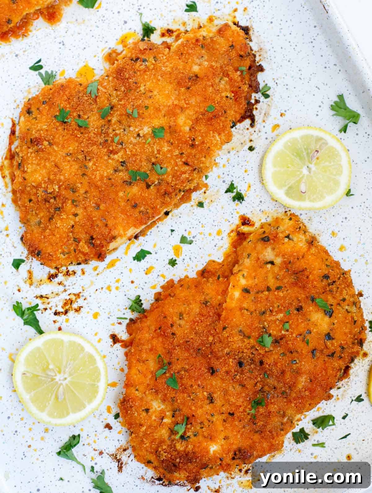 Closeup of golden-brown parmesan and panko crusted chicken cutlets on a baking tray, garnished with fresh parsley.