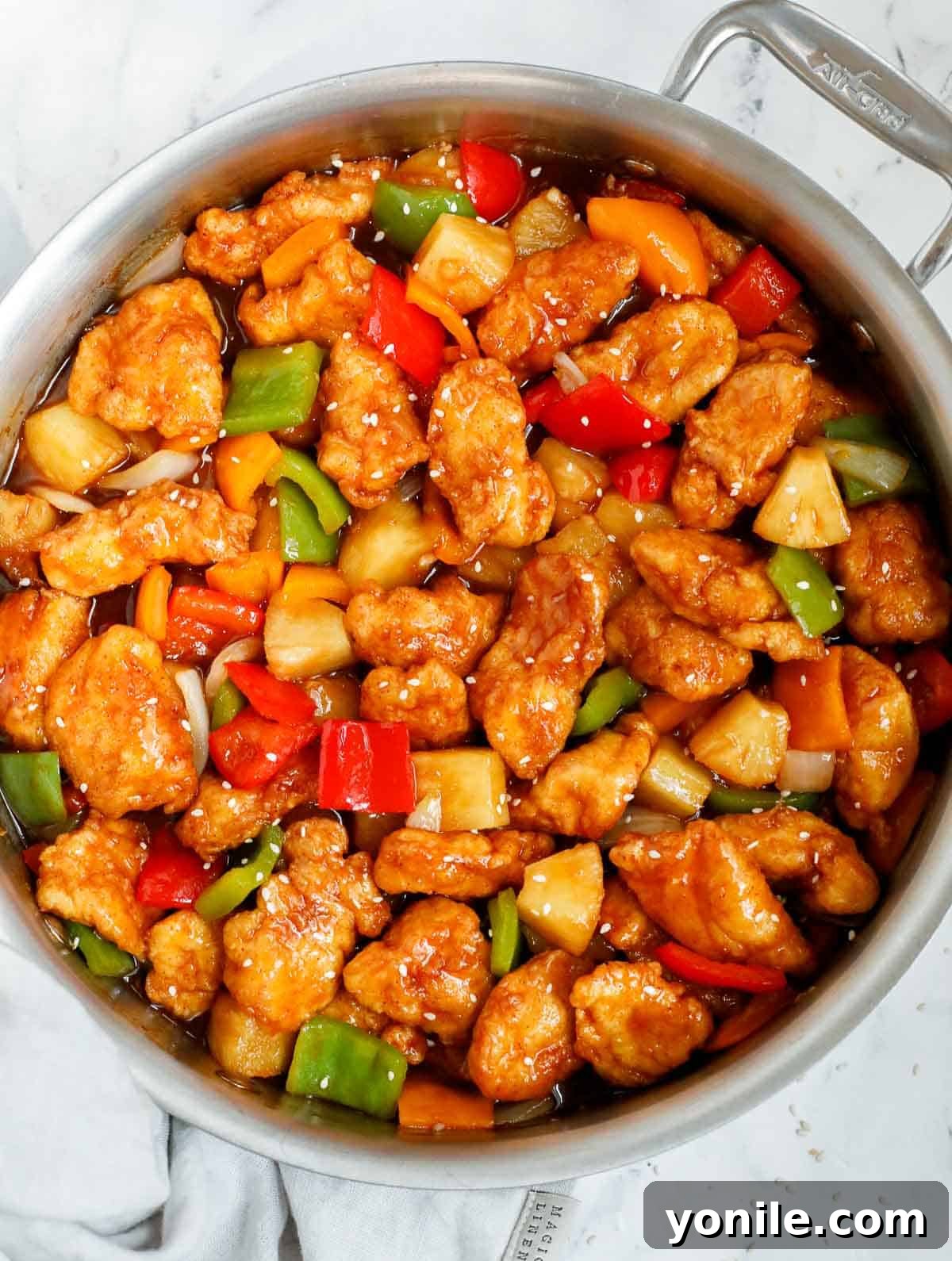 Homemade sweet and sour chicken served in a skillet, garnished with sesame seeds.