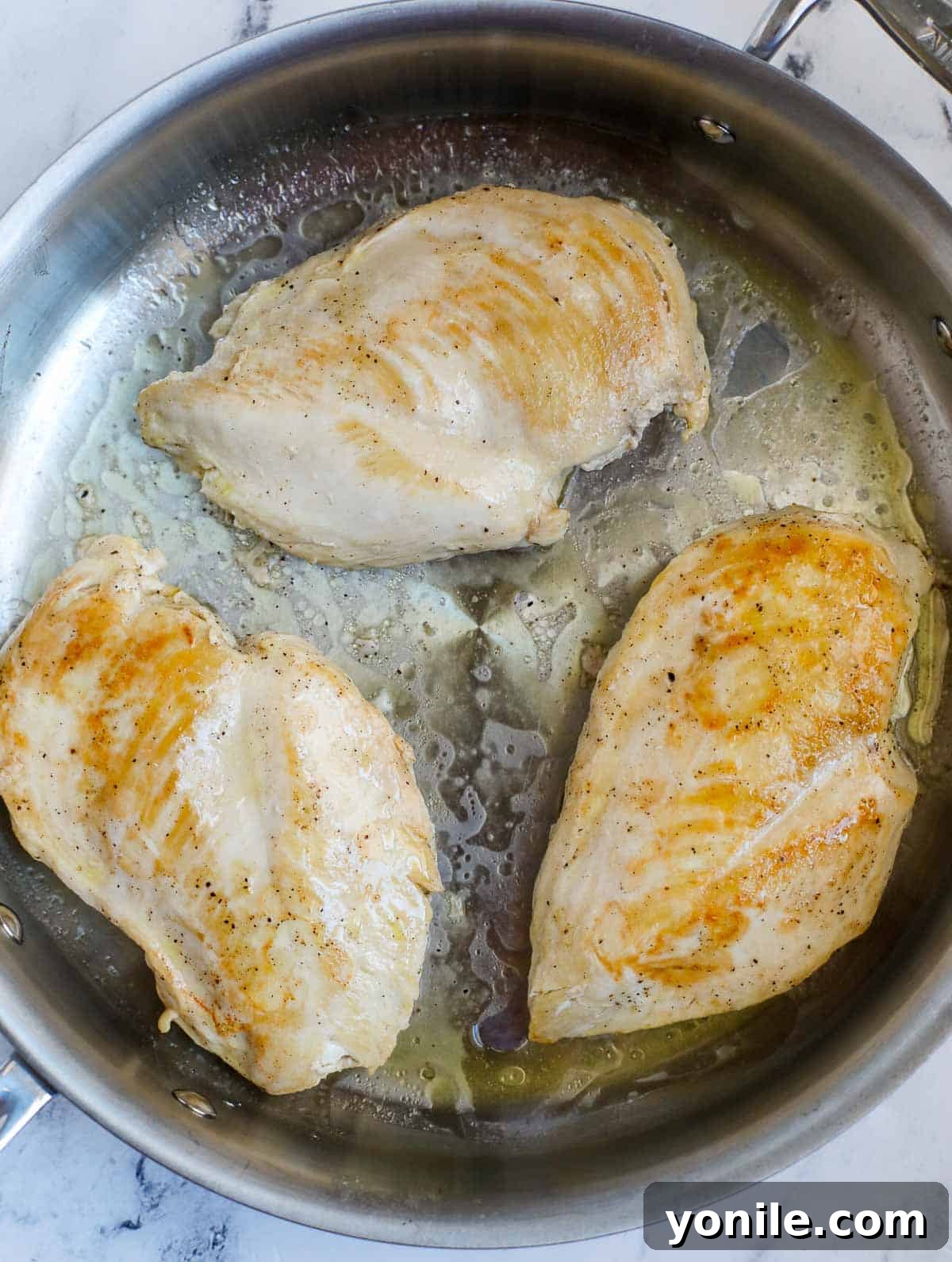 Close-up of chicken breasts searing to a beautiful golden brown in a hot skillet with butter and olive oil.