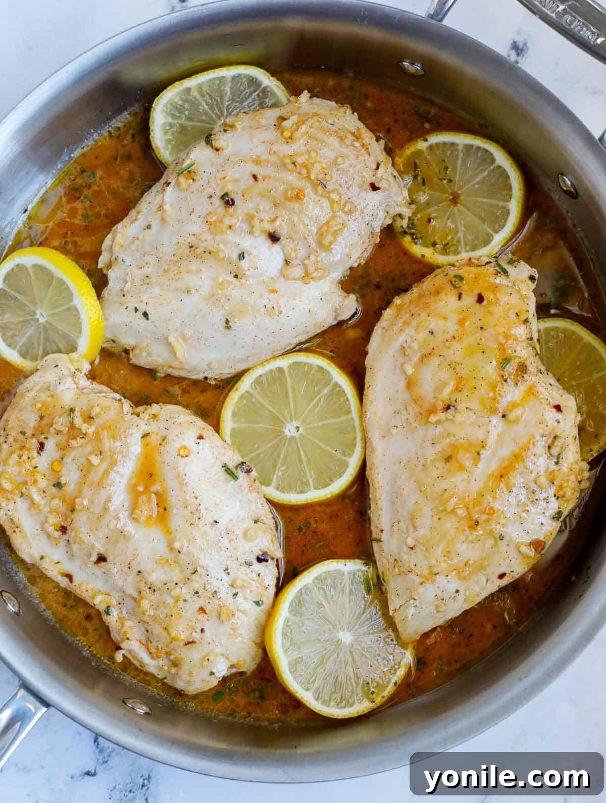 Sizzling pan-seared chicken breasts coated in the lemon rosemary sauce, nestled with fresh lemon slices, ready for the oven.
