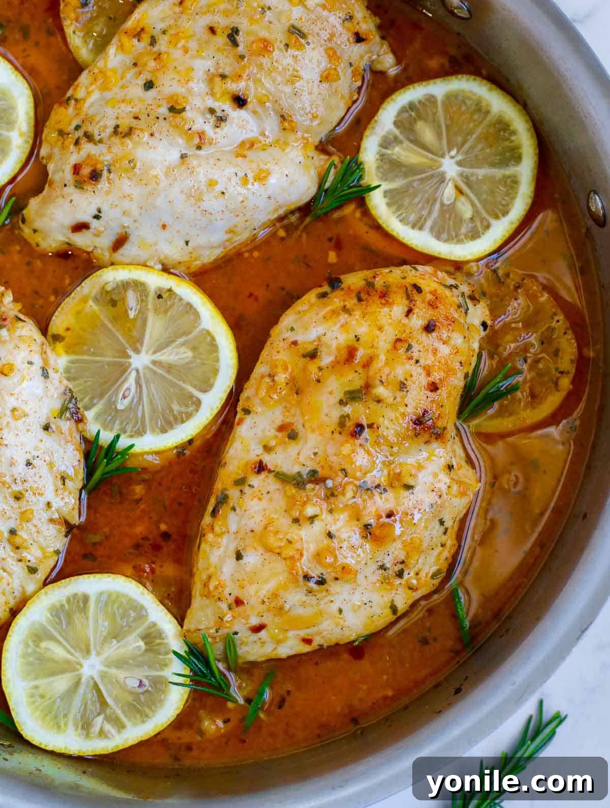 A close-up of a rustic skillet filled with perfectly baked lemon rosemary chicken, showing the glistening sauce and tender chicken.